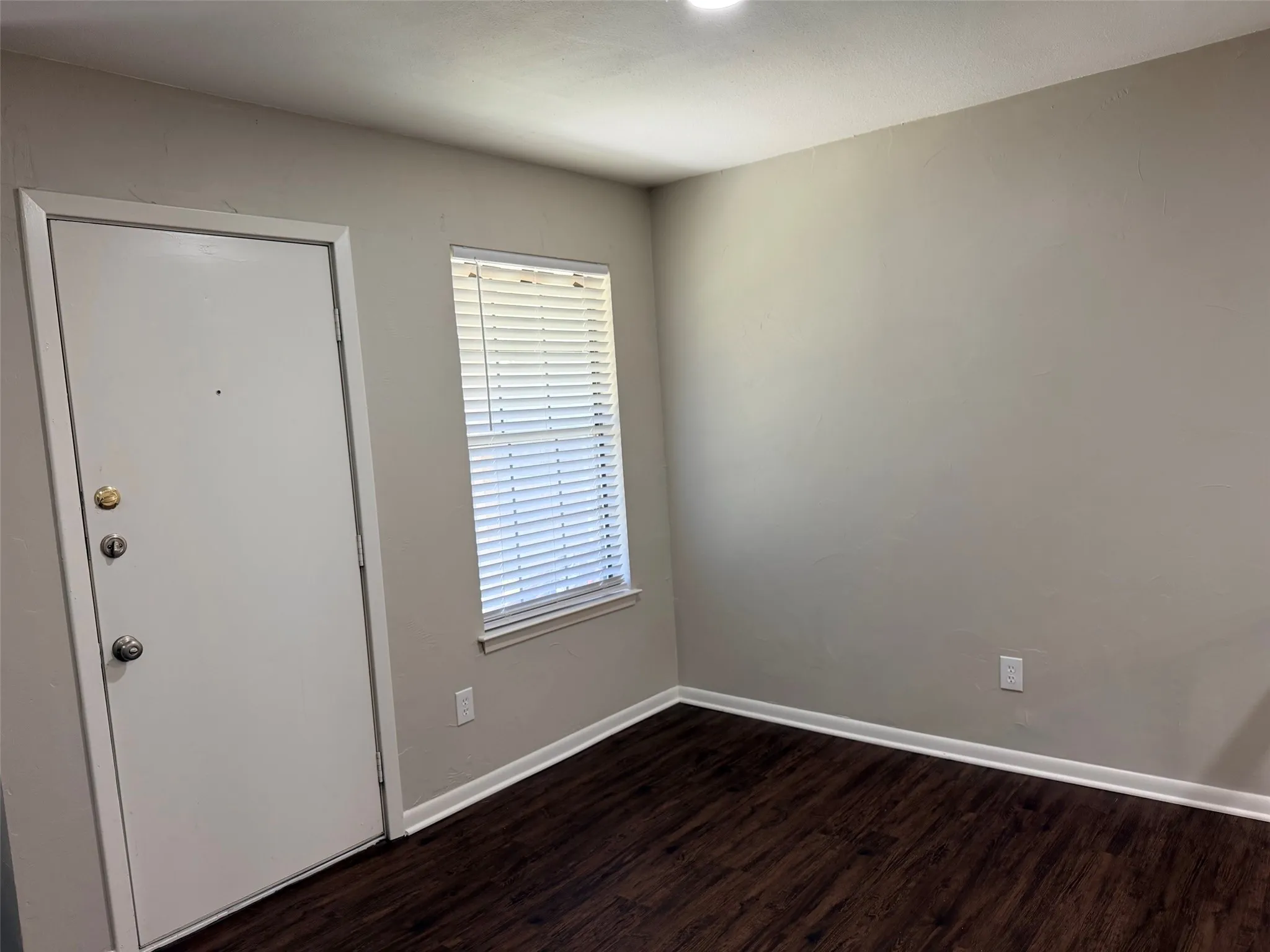 Entry area featuring a solid core door with brass hardware, wood-finish flooring, and light-toned walls
