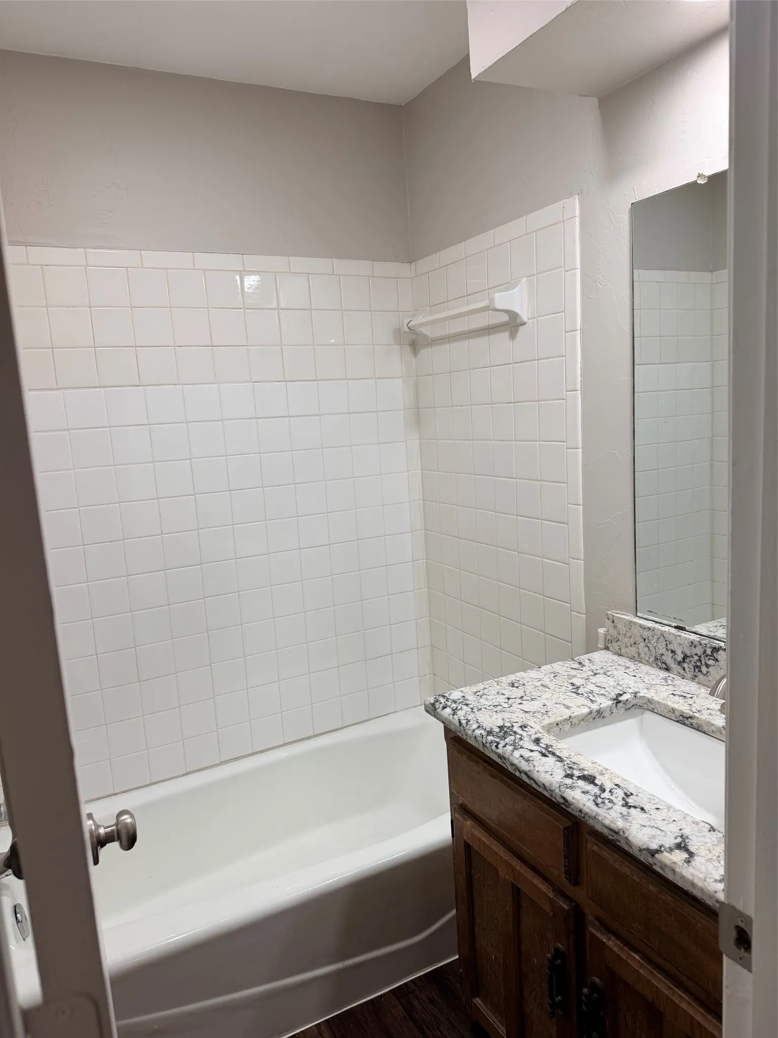 Bathroom featuring a built-in bathtub, white subway tile surround, granite-style countertop, integrated sink, and wood-finish vanity