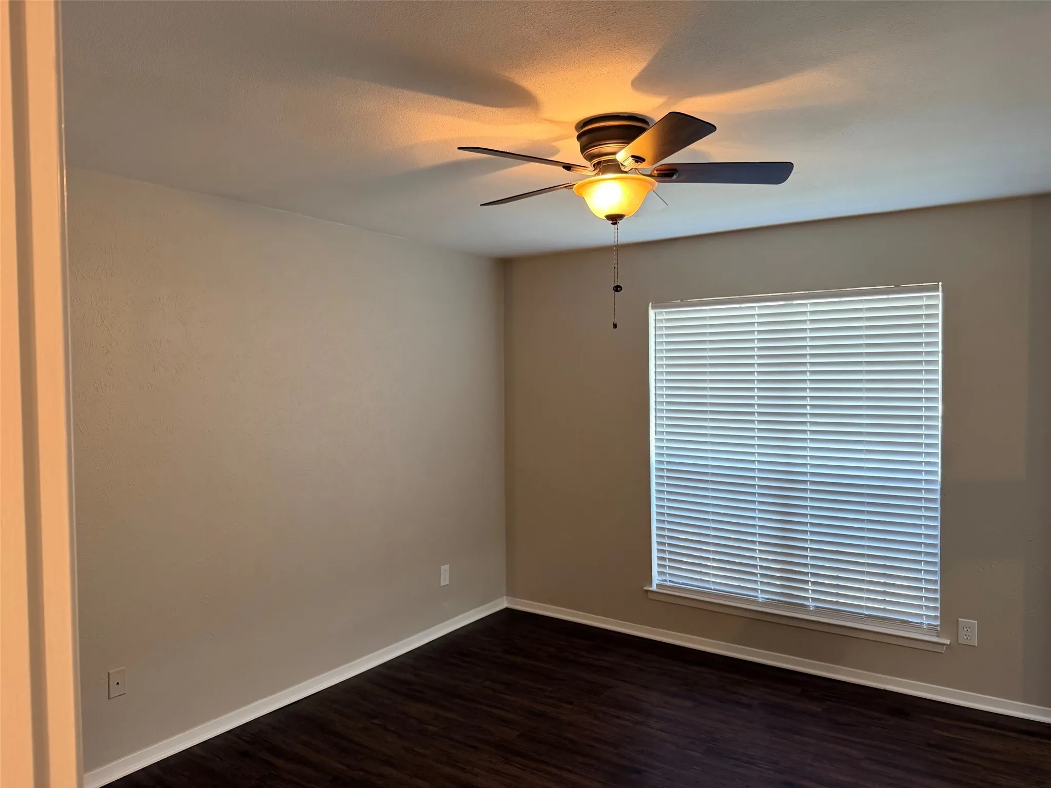 Interior room featuring dark wood-finish flooring, neutral wall paint, and white baseboards