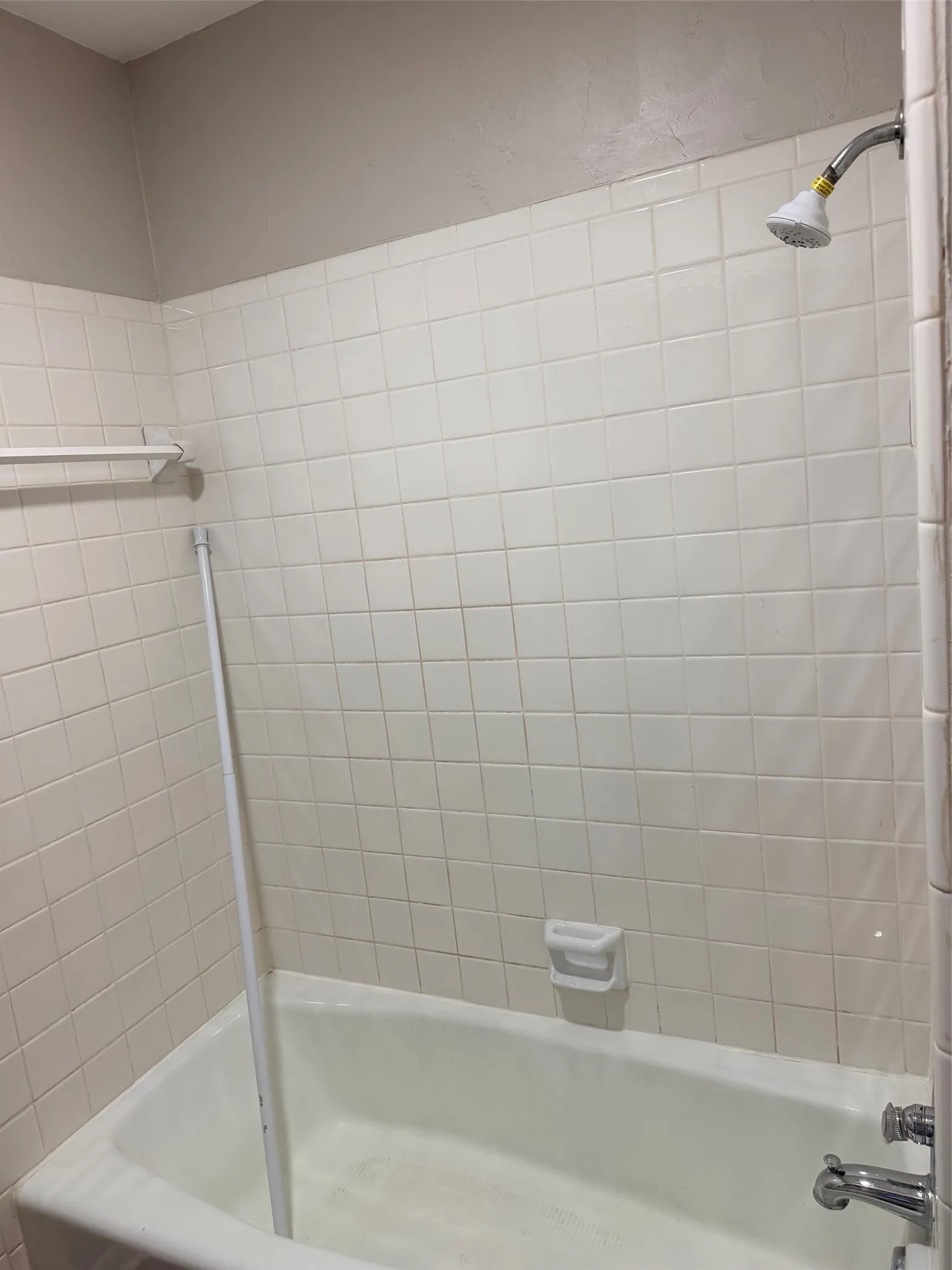 White ceramic tile shower surround with a built-in soap dish, chrome shower head, and matching tub faucet