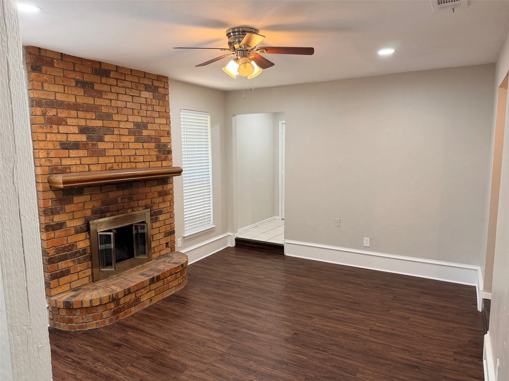 Living area featuring a brick fireplace with a wood mantle, wood-finish flooring, and a ceiling fan with integrated lighting