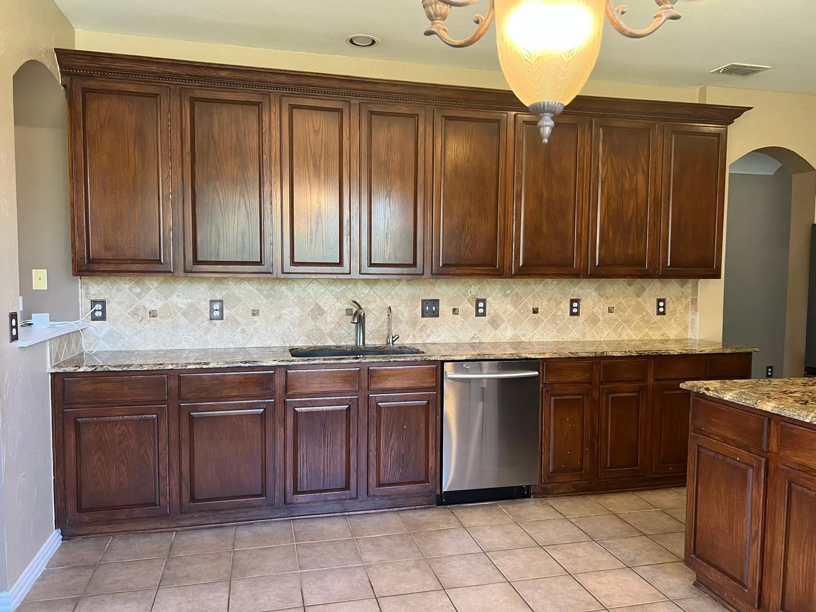 Kitchen featuring extensive dark wood cabinetry, a decorative chandelier, granite countertops, a tiled backsplash, and stainless steel appliances