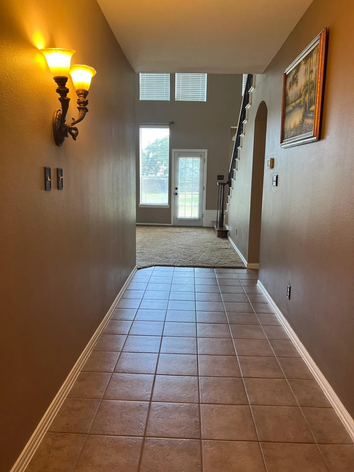 Tiled entryway featuring a decorative wall sconce, leading to a carpeted area with a glass-paneled door