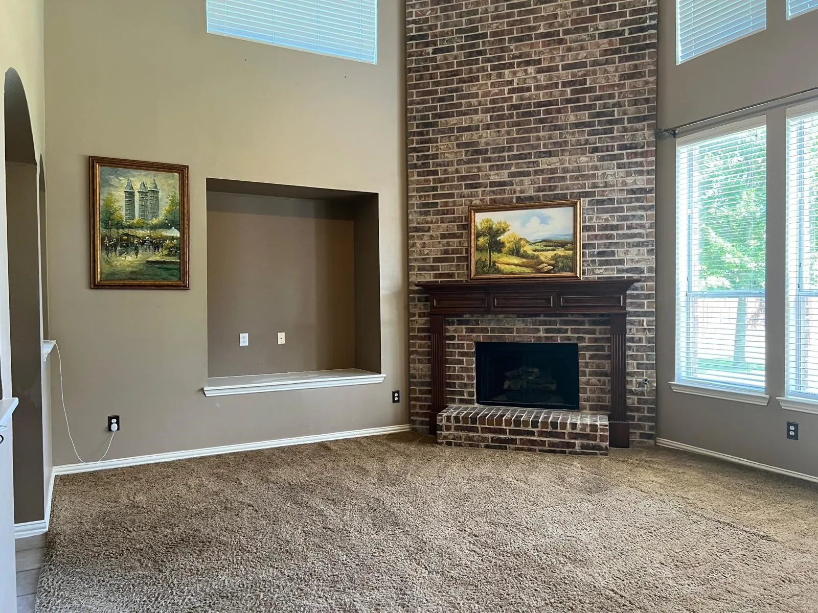 Vaulted ceiling living space featuring a floor-to-ceiling brick fireplace with a wood mantle, a built-in media niche, and large windows with integrated blinds