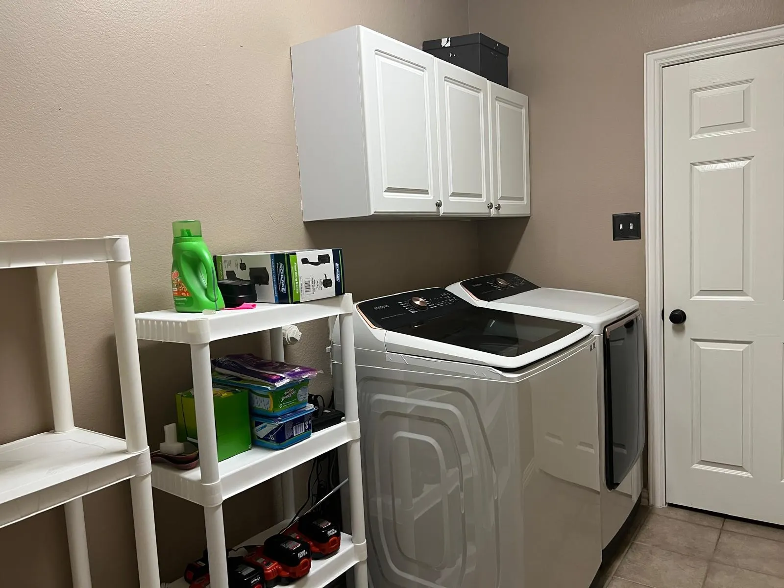 Dedicated laundry space featuring upper white cabinetry, a paneled door with black hardware, and neutral-toned wall paint