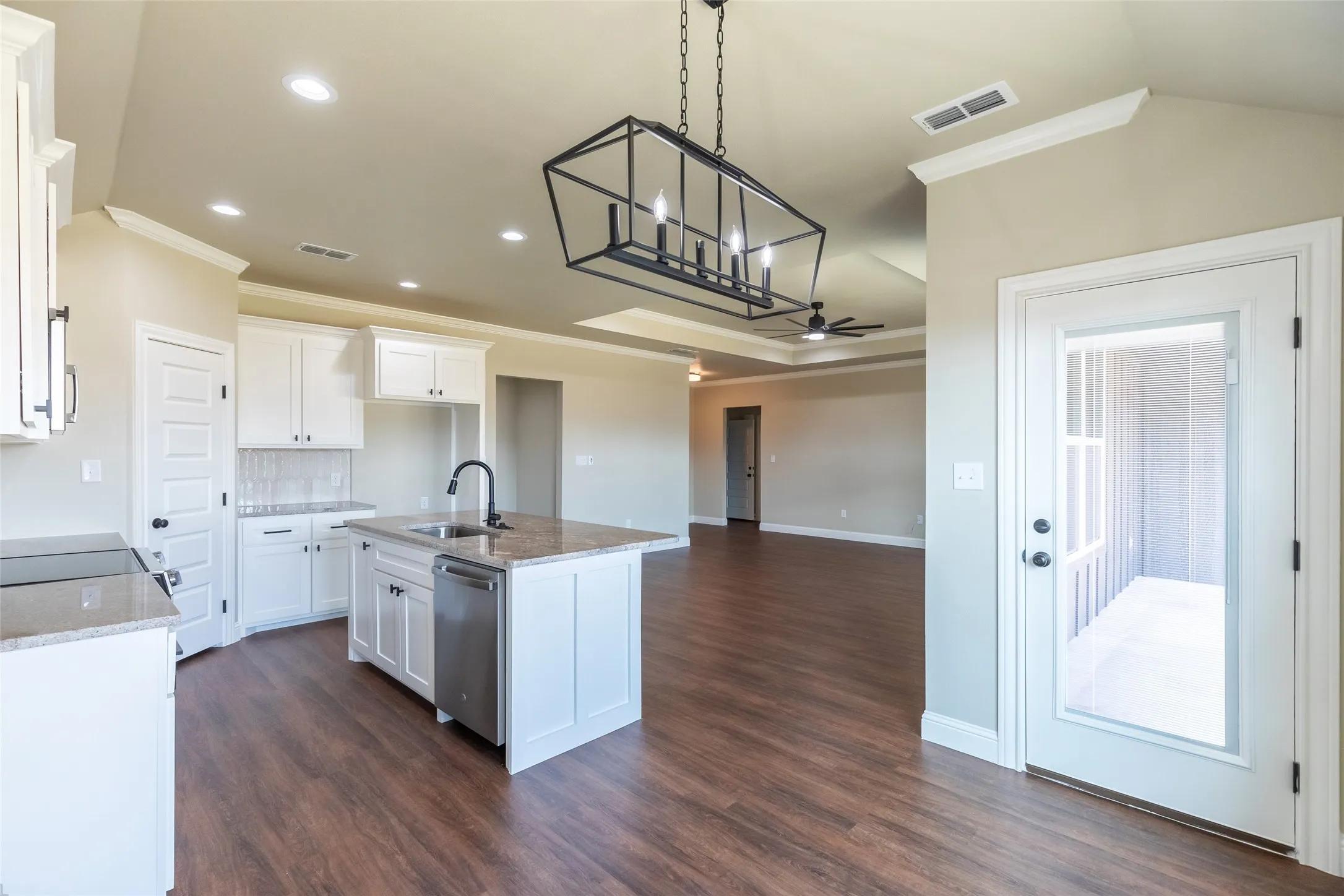 Open-concept kitchen featuring white cabinetry, a central island with a sink, stainless steel dishwasher, and stone countertops