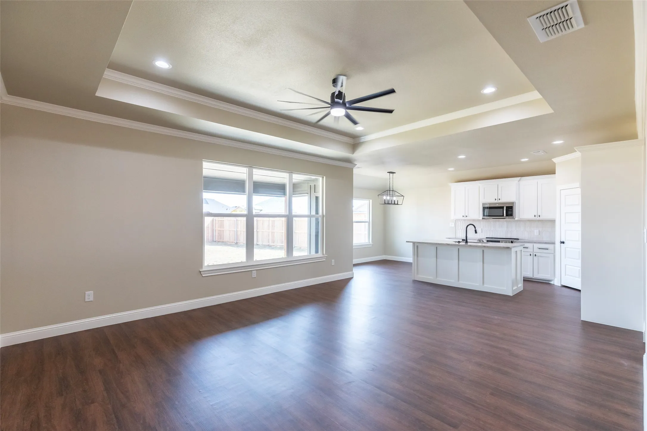 Open-concept living space featuring wood-finish flooring, a tray ceiling with recessed lighting and a ceiling fan, and large windows