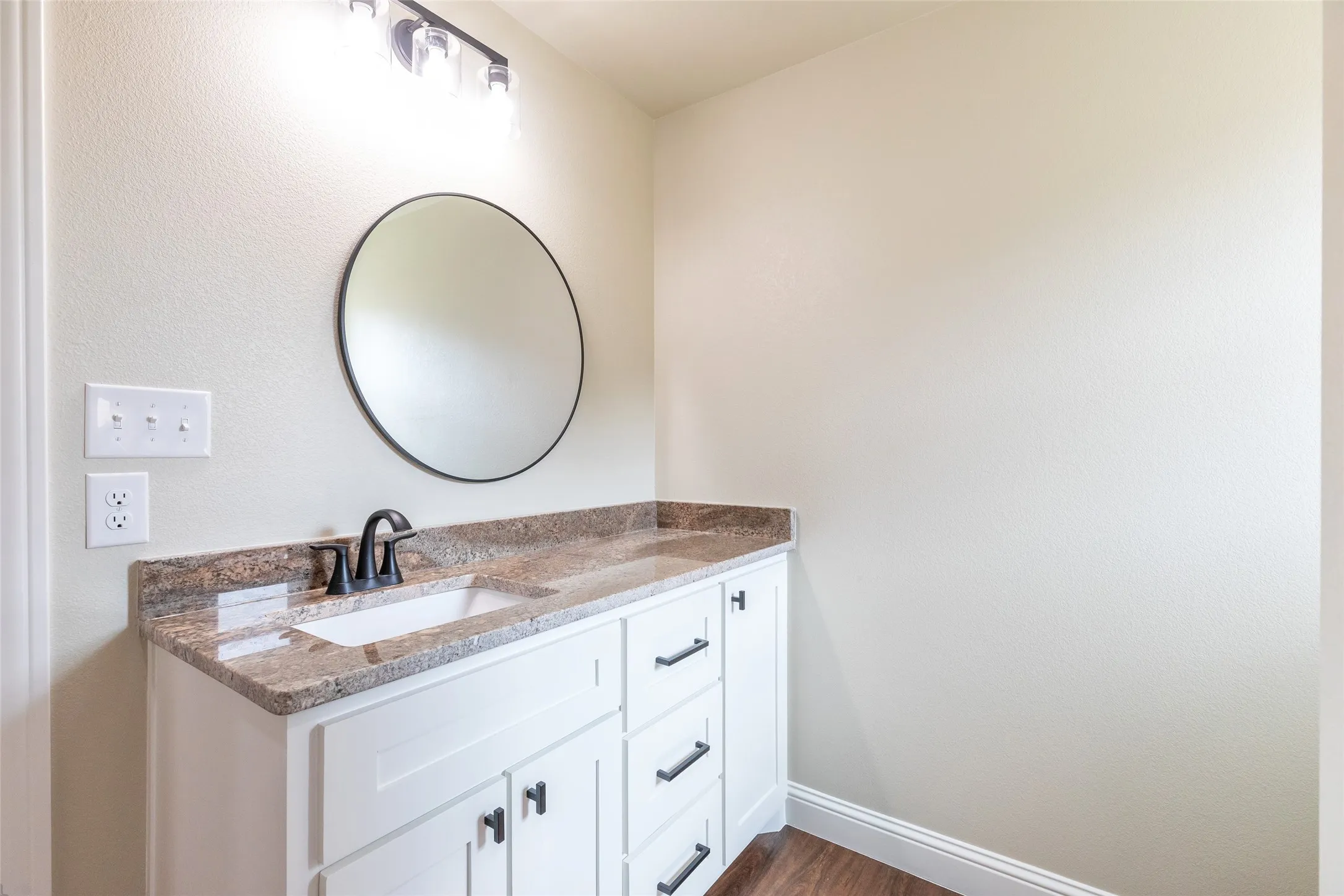 Bathroom vanity featuring a granite countertop, undermount sink, and matte black hardware