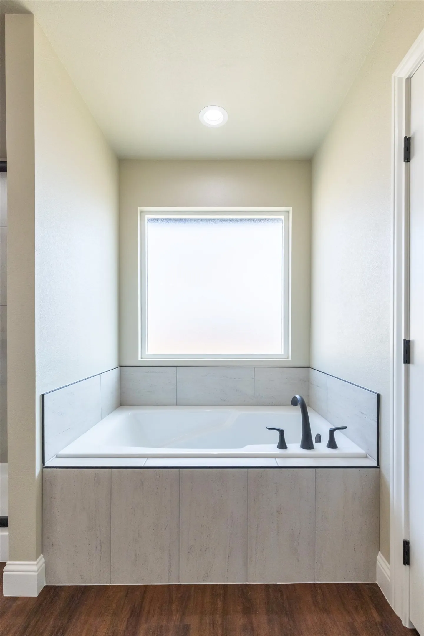 Built-in soaking tub featuring matte black fixtures, set within a tiled surround, under a frosted privacy window