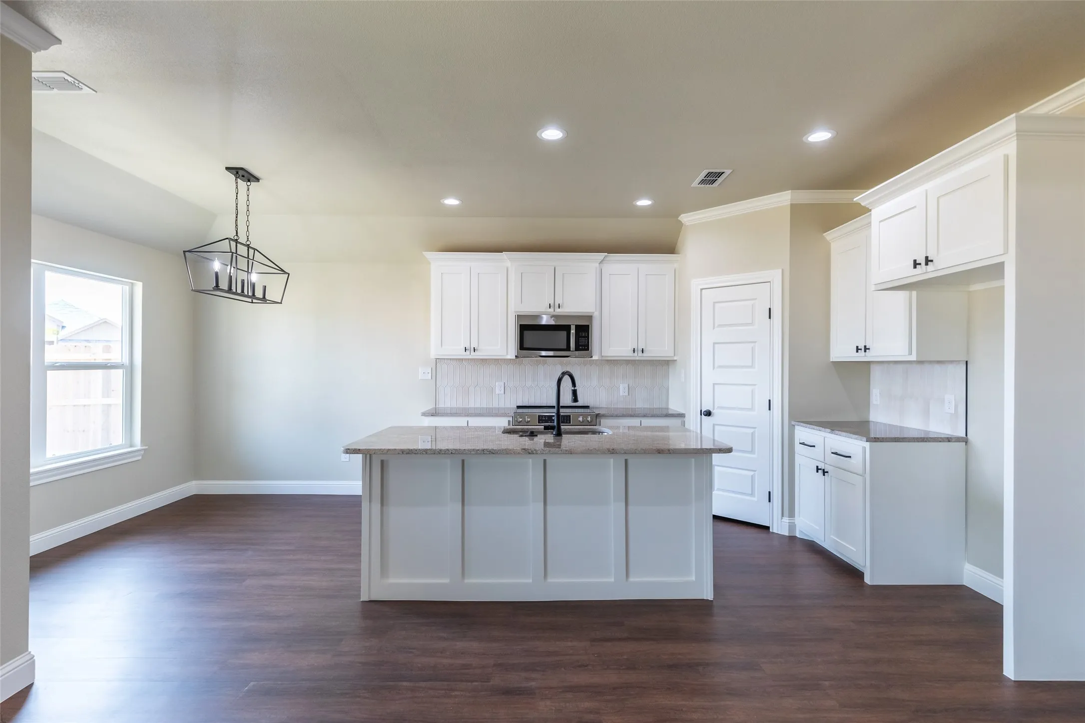 Open-concept kitchen and dining area featuring a central island with sink, white shaker cabinetry, stone countertops, and wood-finish flooring
