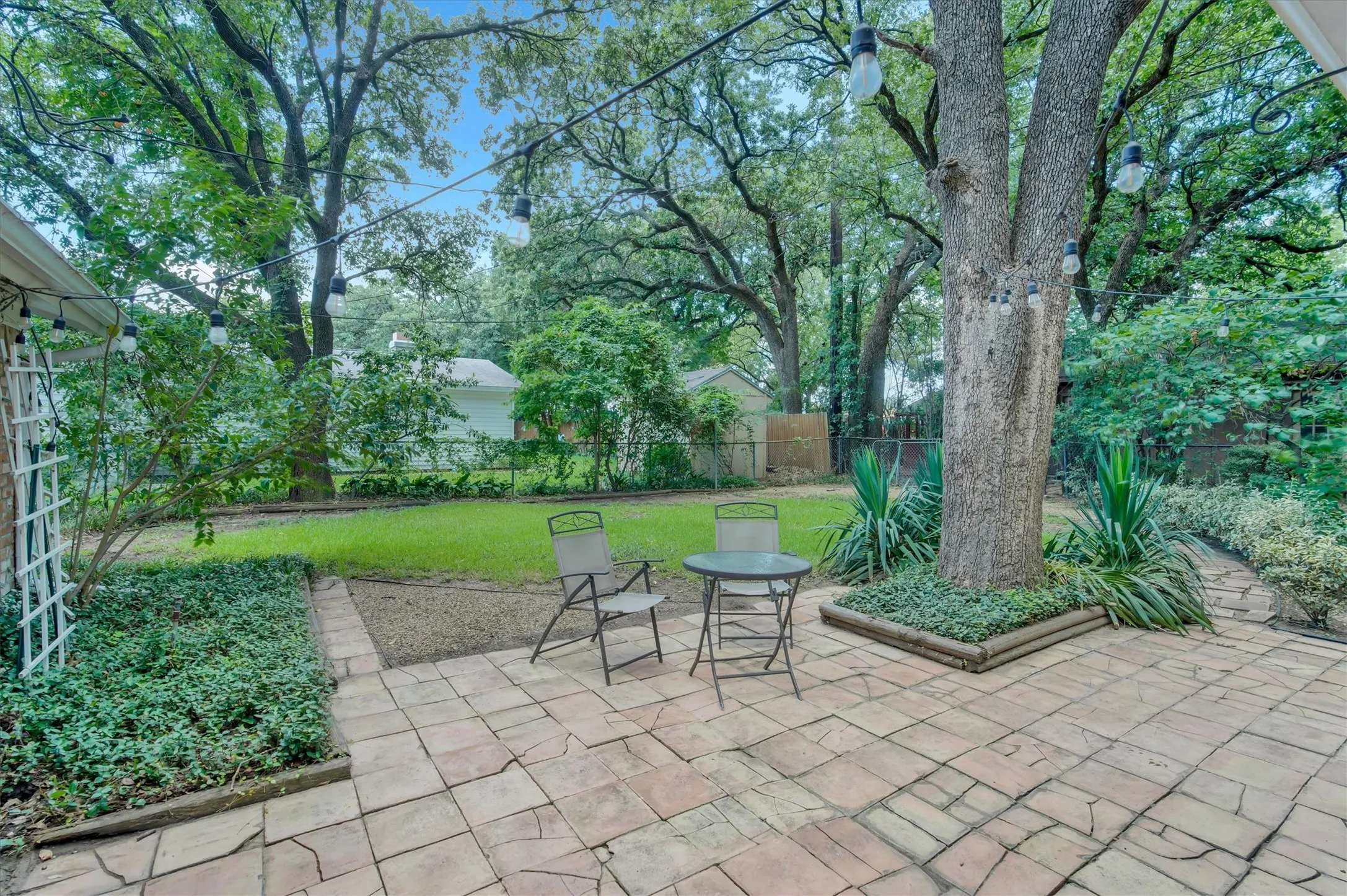 Expansive outdoor patio with large format pavers, featuring mature trees providing shade