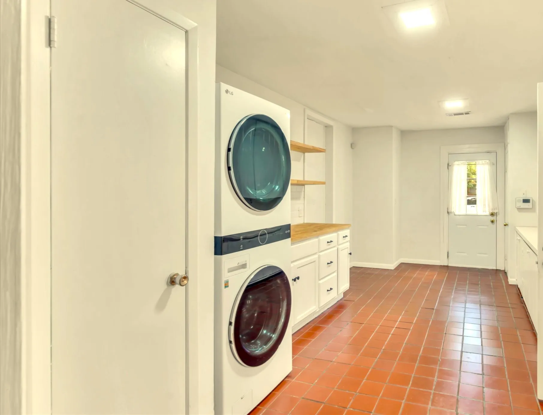  Large laundry area featuring terracotta-style tile flooring, stackable washer and dryer, built-in cabinetry with wood-finish countertops, and open shelving