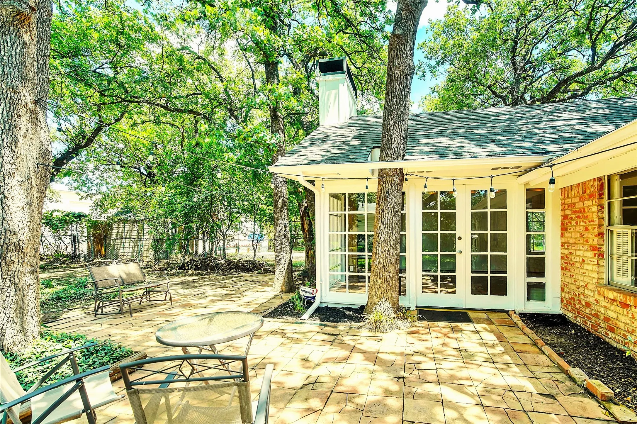 Paved patio area featuring extensive brickwork, mature trees, and a direct entrance via multiple glass-paneled French doors