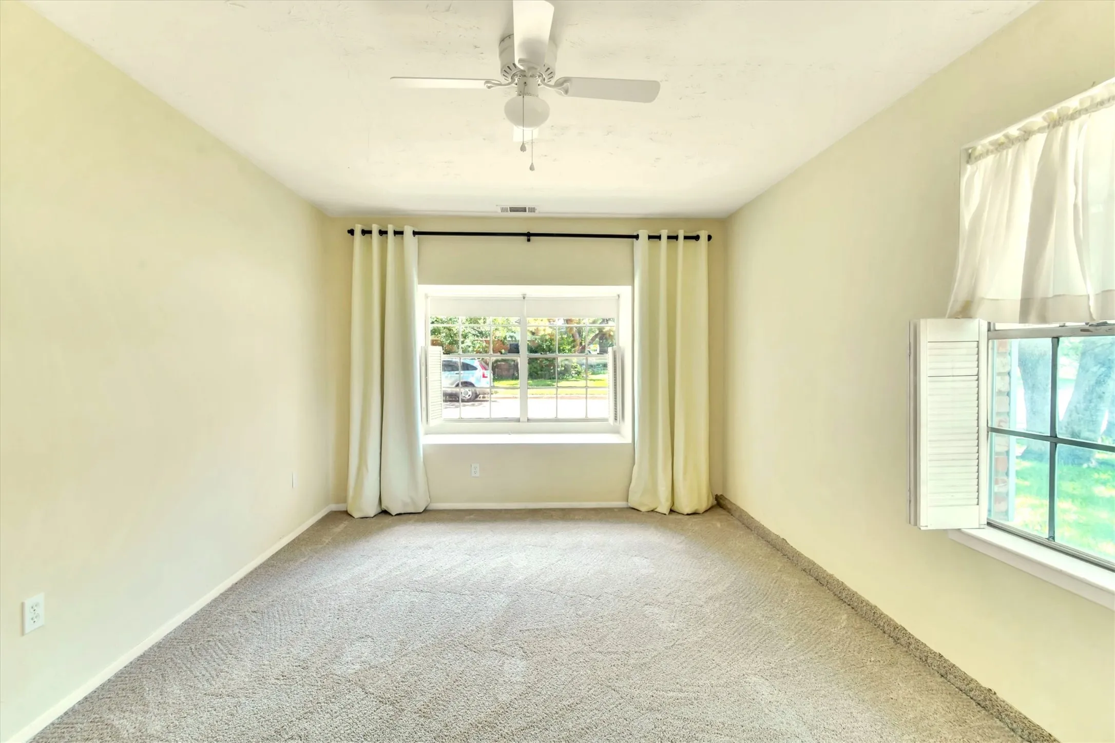 Room featuring a window seat, light-toned carpeting, and a ceiling fan