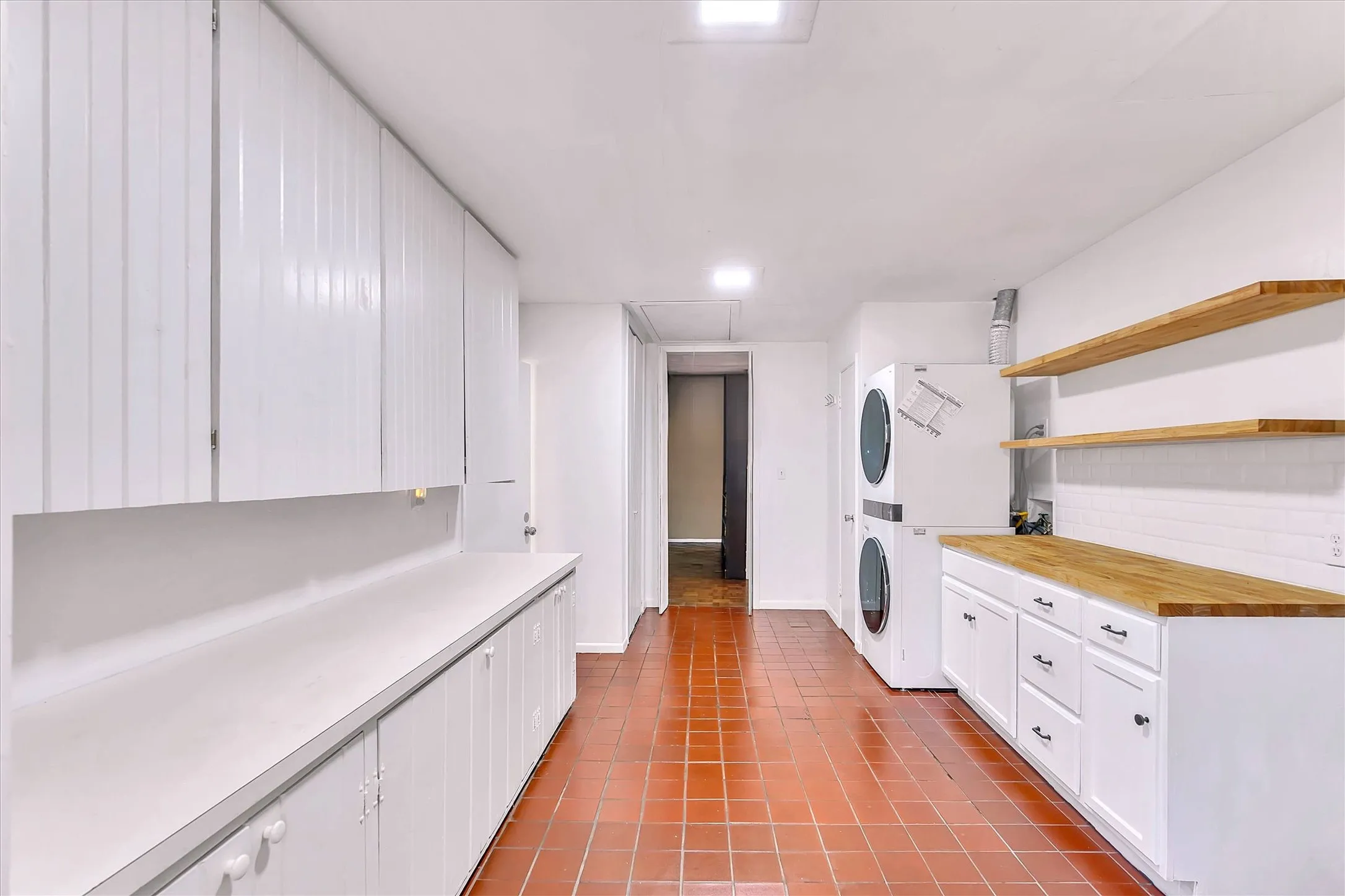 Laundry area featuring terracotta tile flooring, extensive white cabinetry, light wood-finish countertops, and white subway tile backsplash