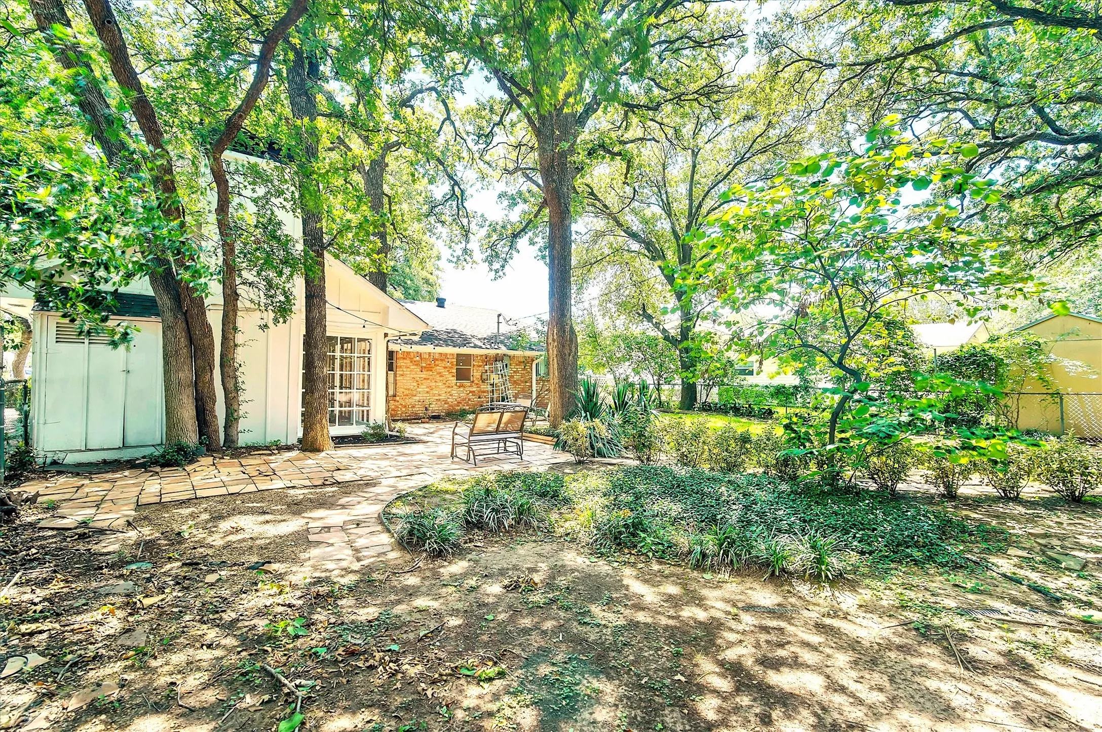 Expansive outdoor space featuring a stone patio, mature trees, shrubbery, and a lush​​‌​​​​‌​​‌‌​‌‌​​​‌‌​‌​‌​‌​​​‌​​ lawn