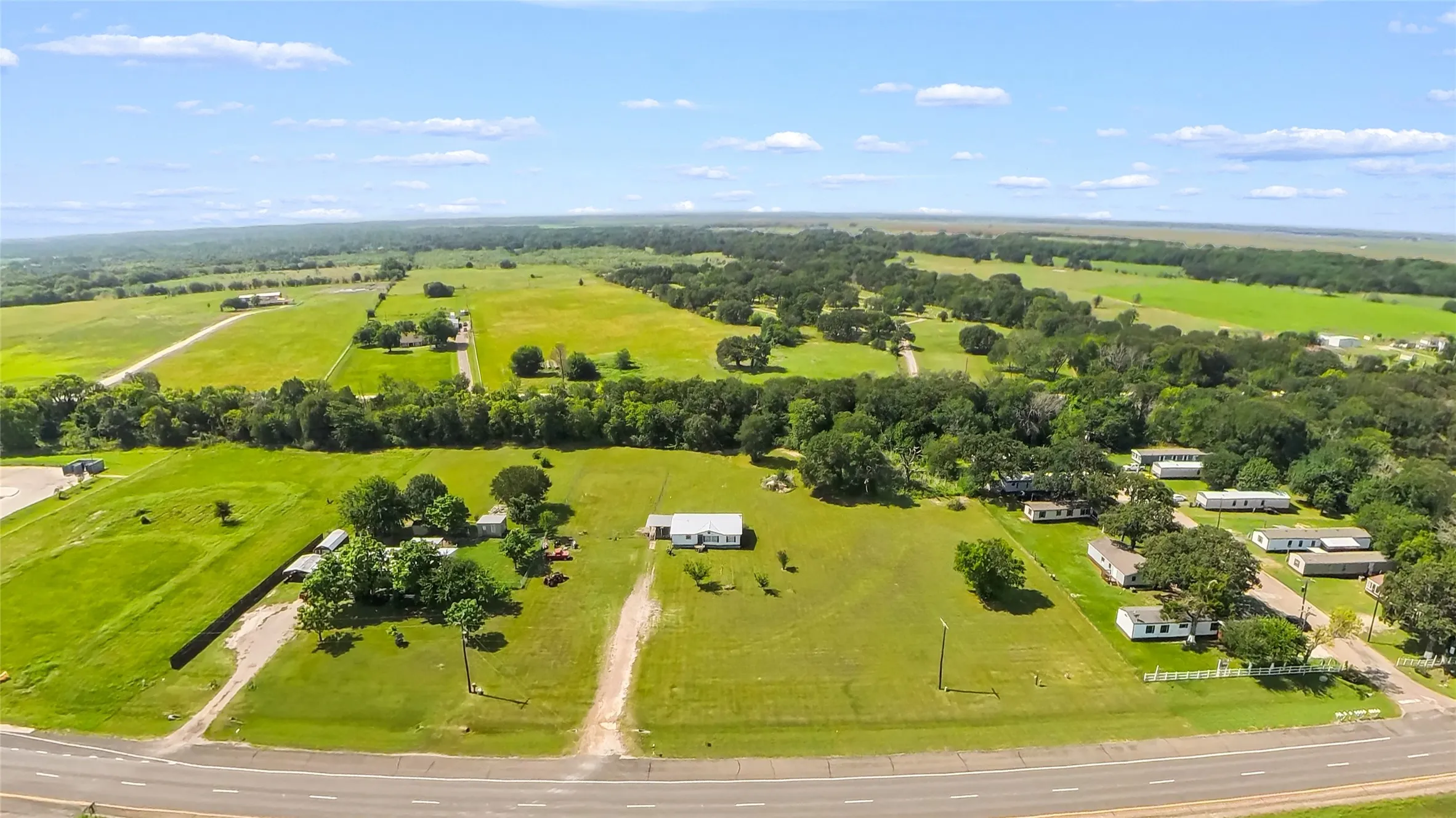 Expansive land parcel featuring open green fields, mature trees, and multiple structures