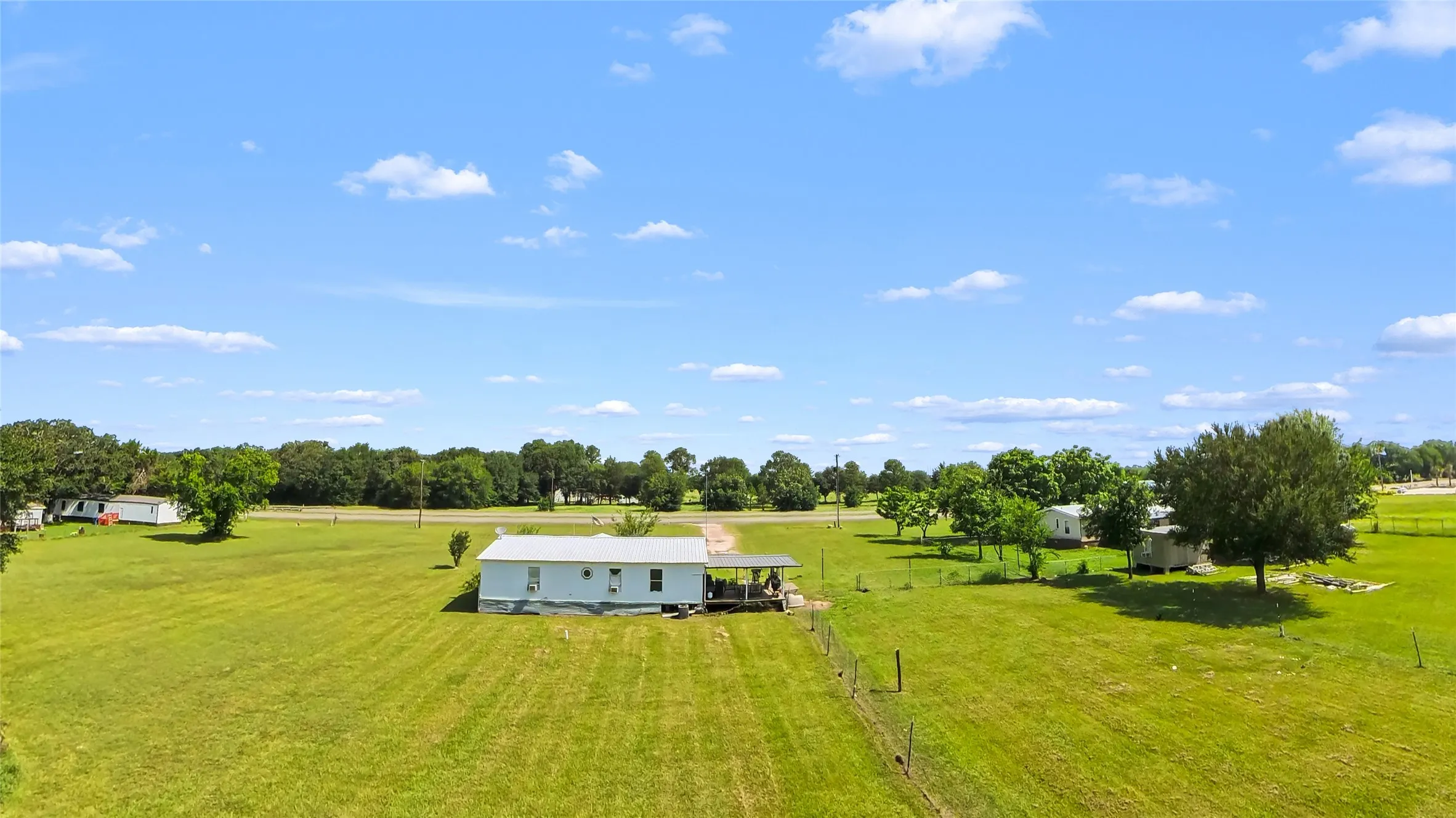 Expansive green acreage with a single-story residence featuring a light-colored exterior and a metal roof