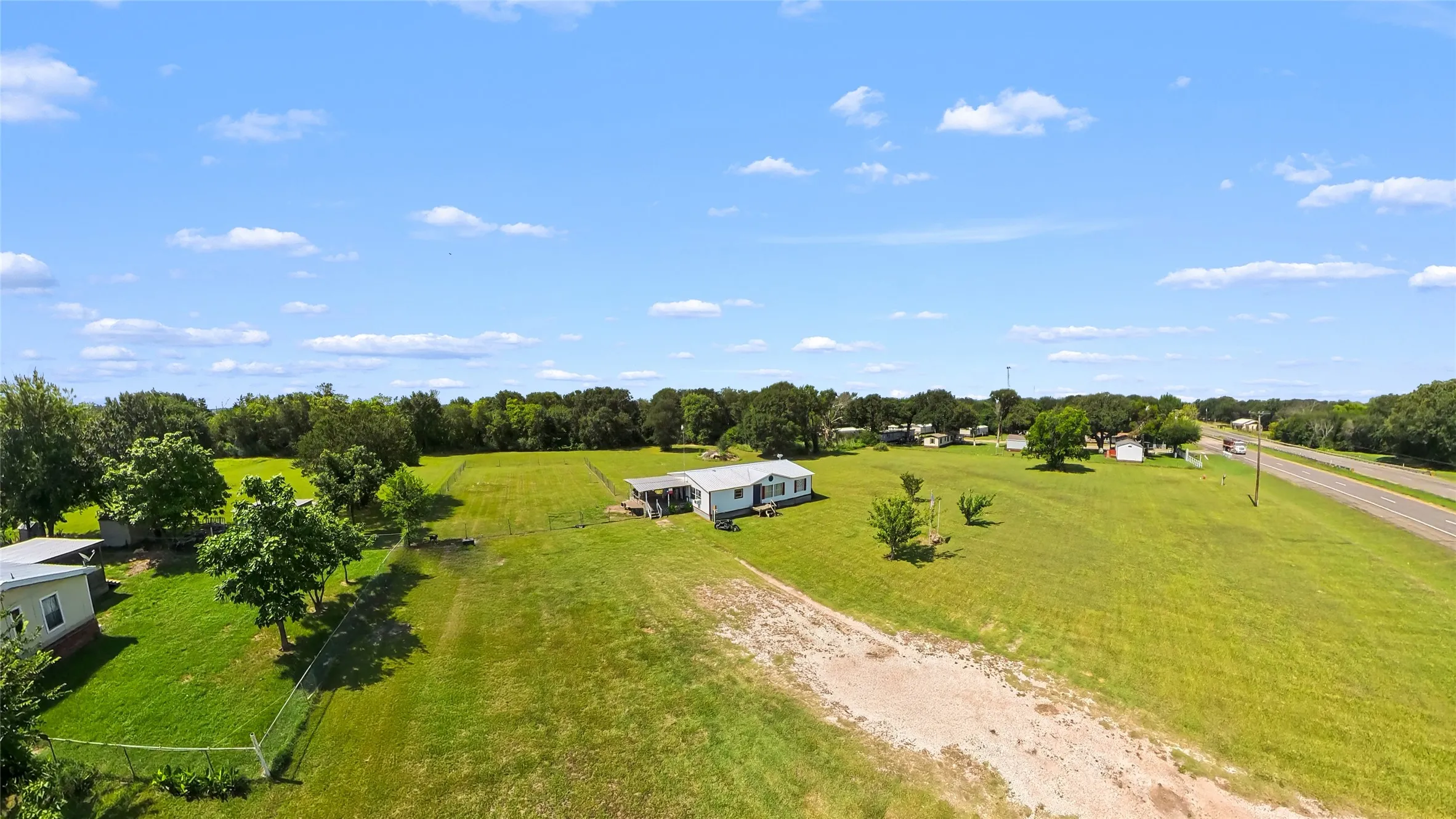 Expansive green acreage with a single-story dwelling, mature trees, and a visible roadway