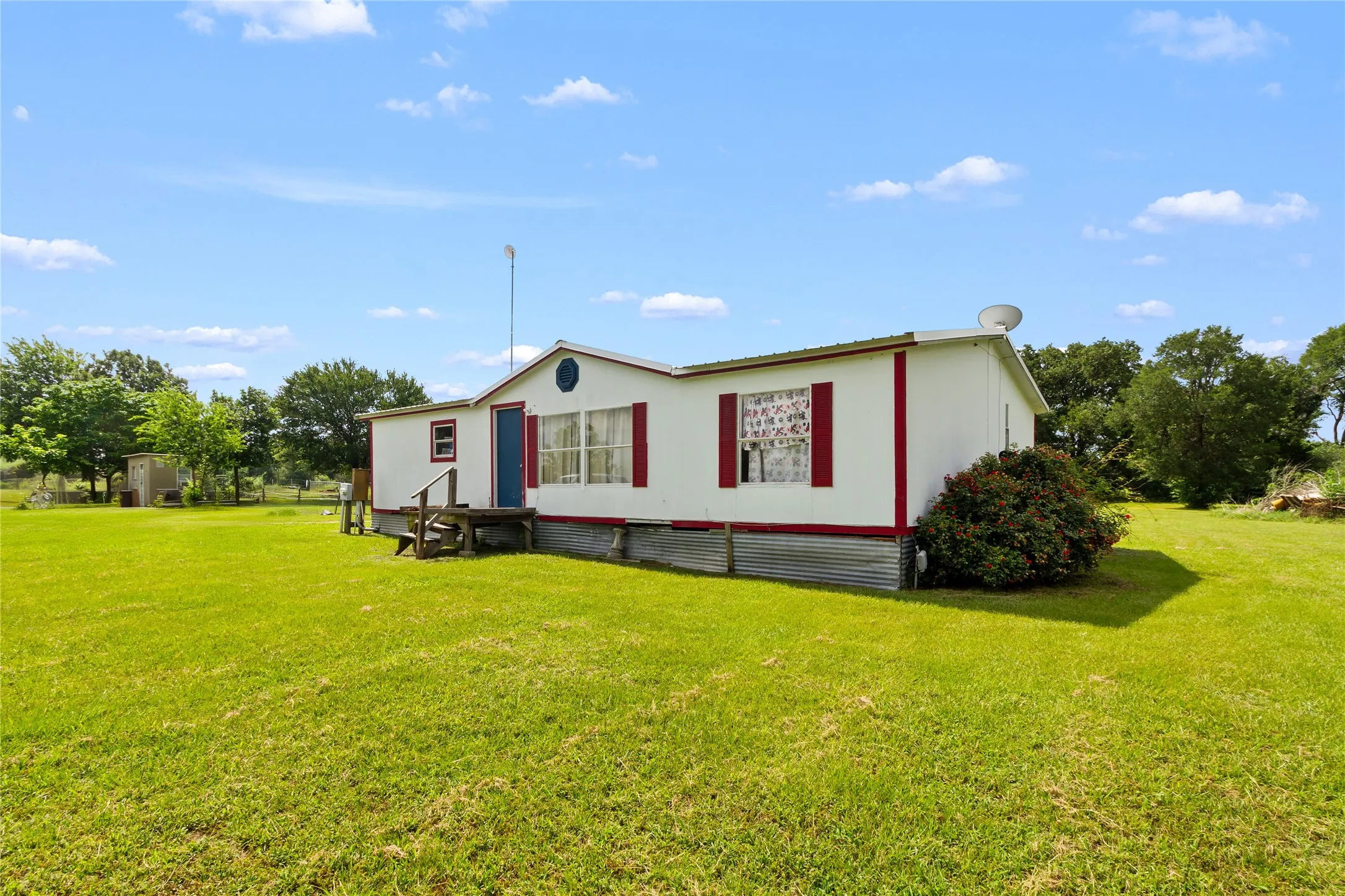 White manufactured home with red trim, a blue entry door, and a front wood deck