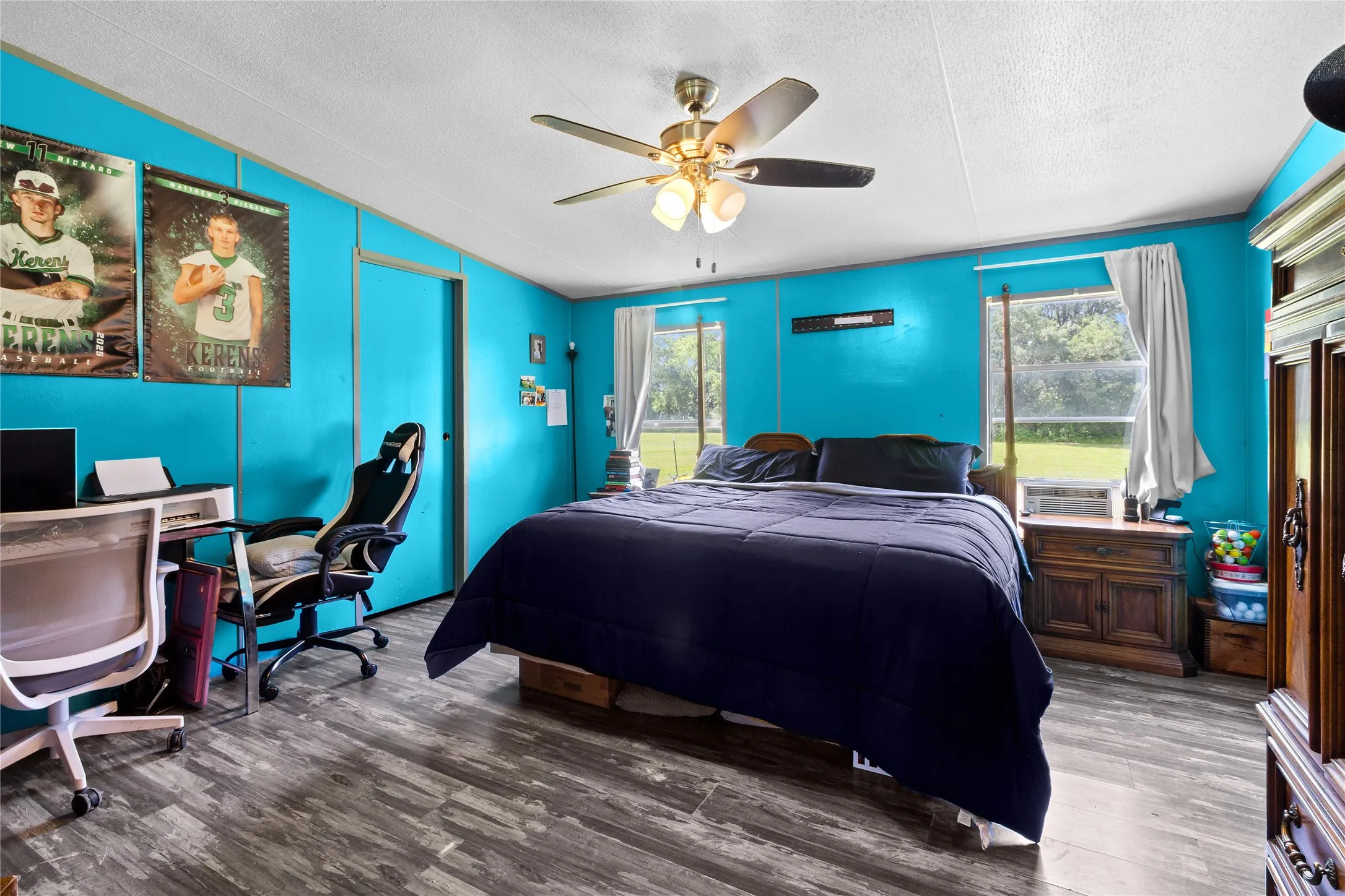 Spacious room featuring wood-finish flooring, a ceiling fan, and multiple windows providing natural light