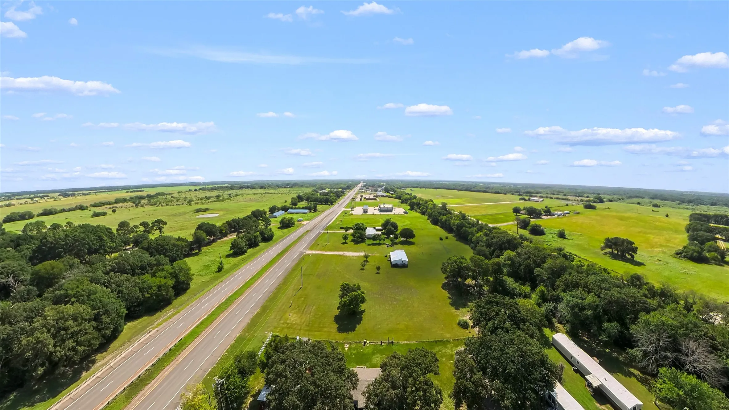 Expansive rural property featuring a long stretch of highway frontage, mature trees, and open green fields