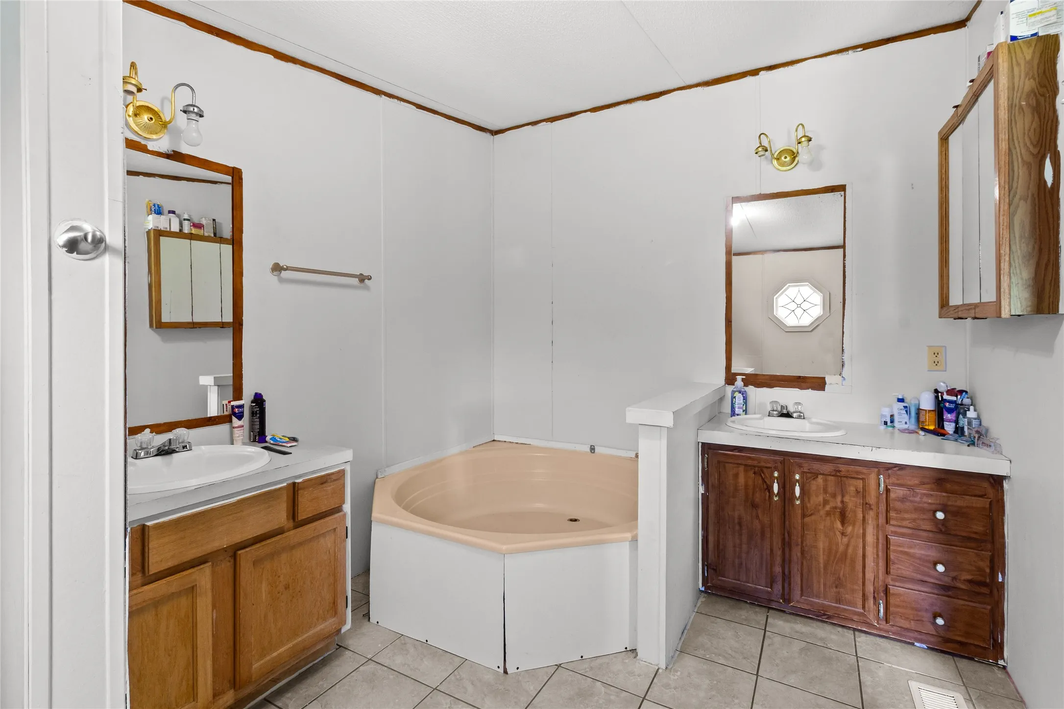 Bathroom featuring a corner soaking tub, dual vanities with integrated sinks, wood-finish cabinetry, and tiled flooring