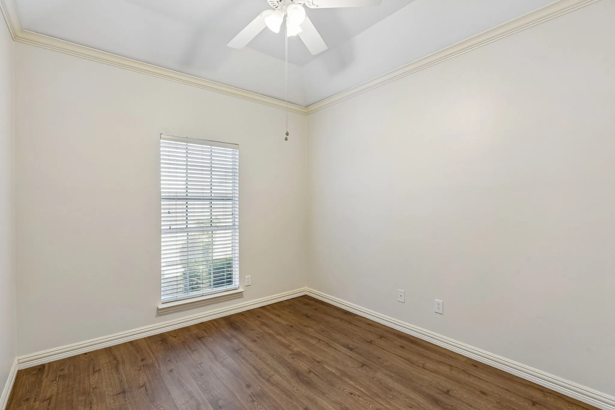 Spacious room featuring wood-finish flooring, a ceiling fan, crown molding, and neutral wall tones
