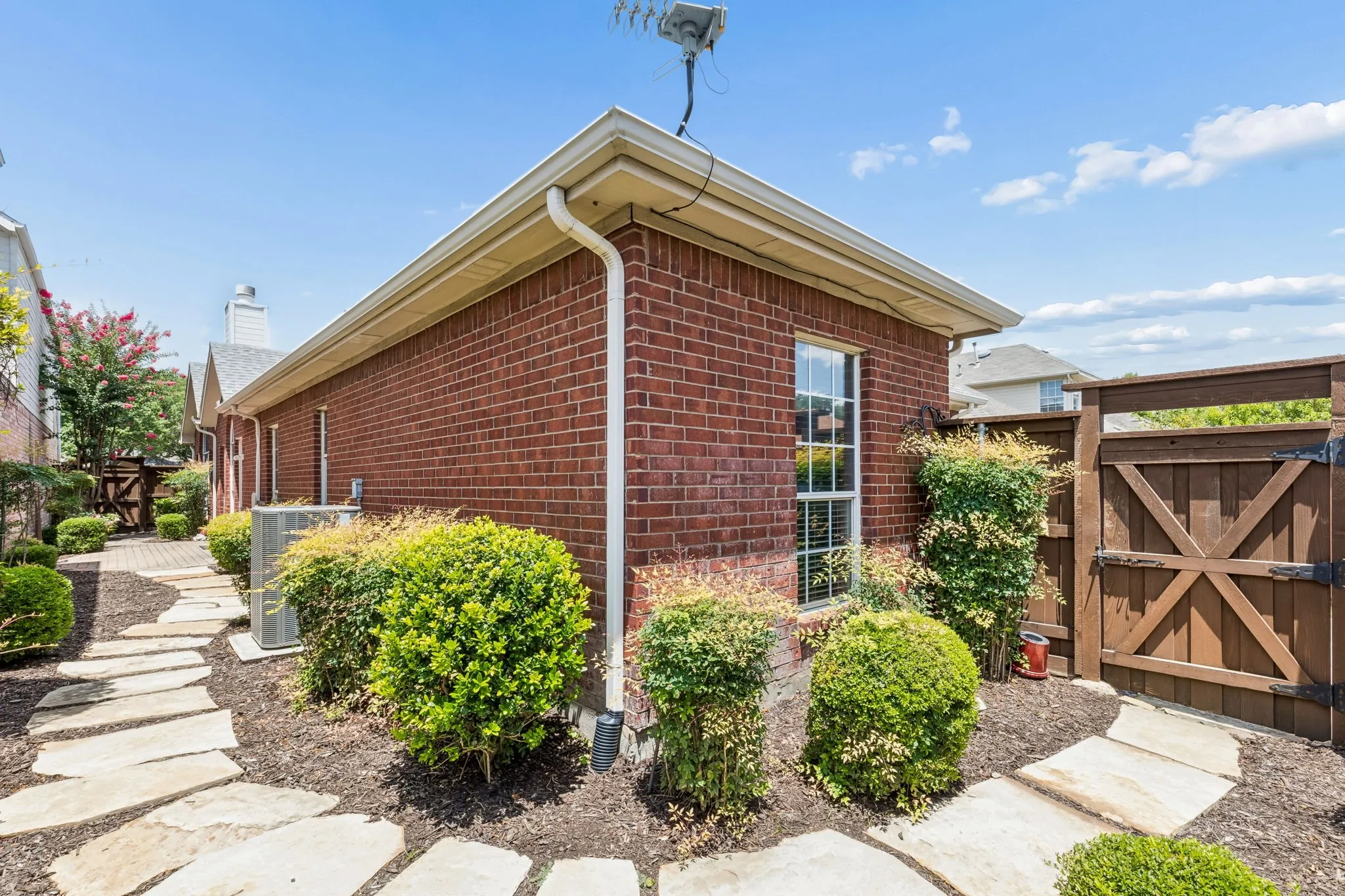Brick exterior featuring a wood fence, flagstone pathway, and mature landscaping
