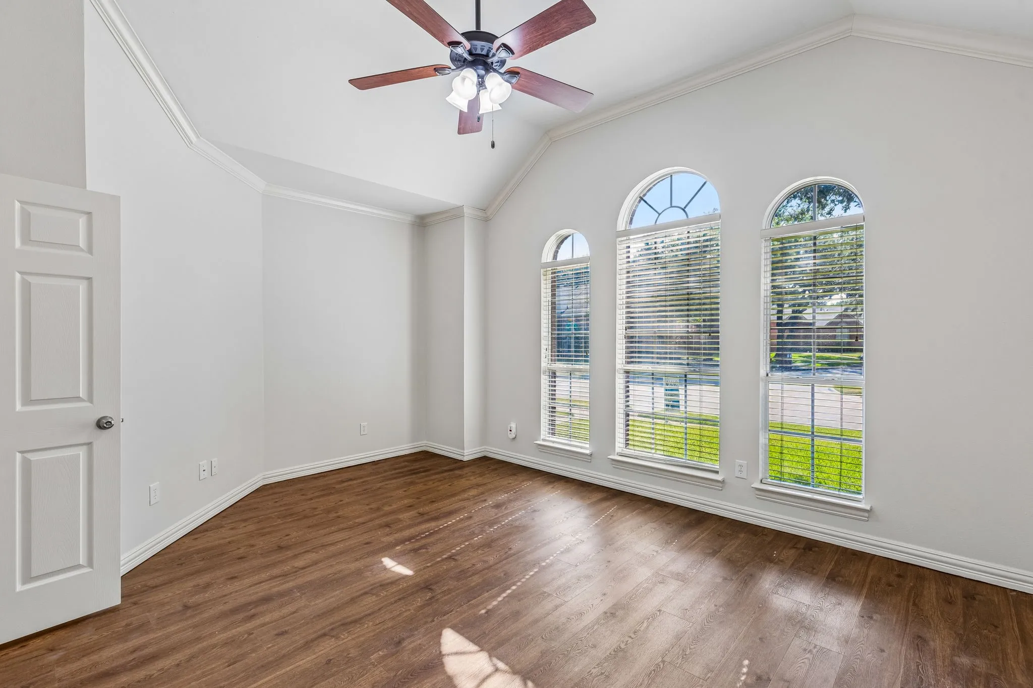 Bright and spacious room showcasing soaring vaulted ceilings, rich wood-finish flooring, and three sets of French doors with arched transom windows flooding the space with natural light