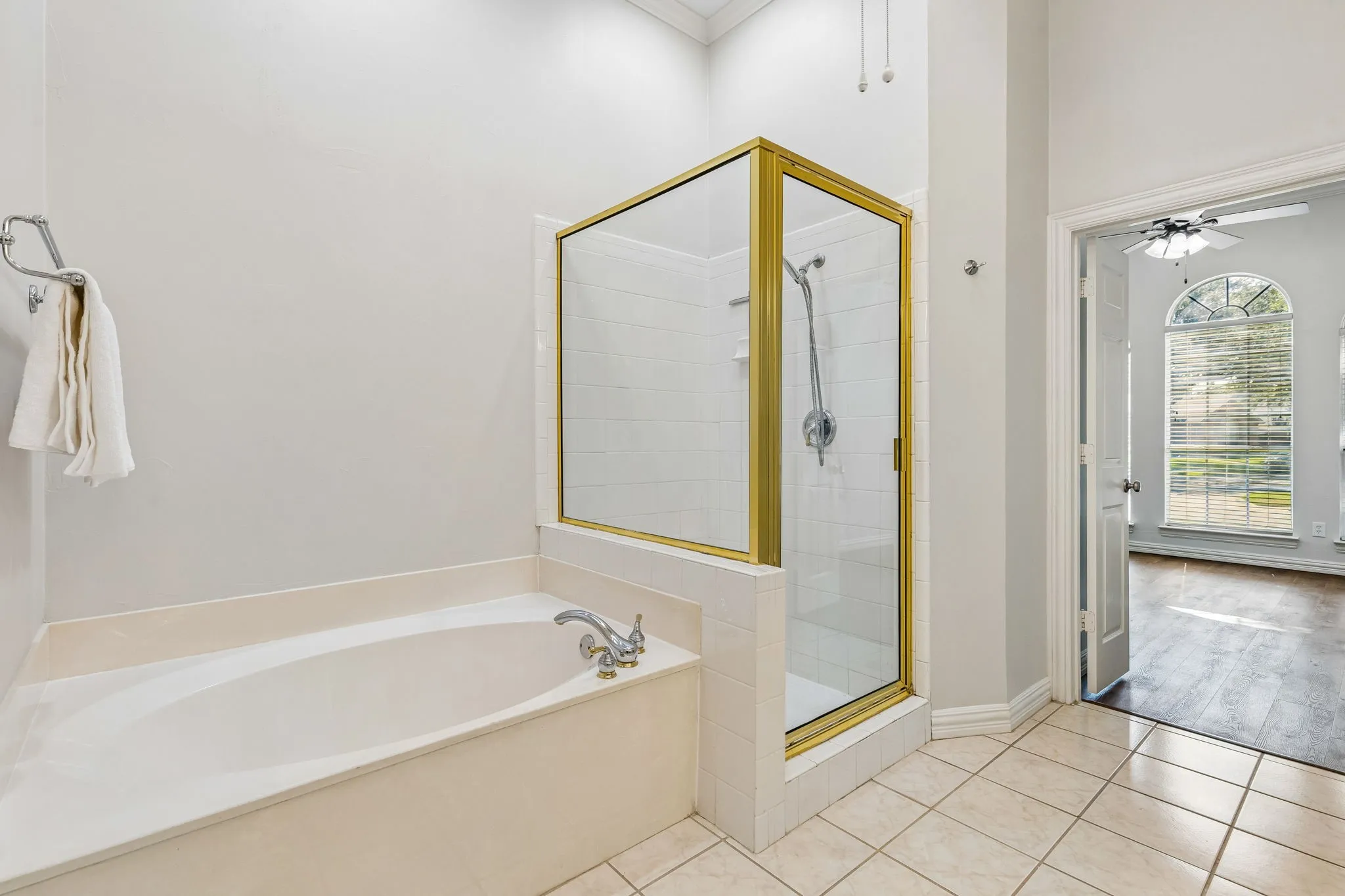 Bathroom featuring a built-in soaking tub, a stand-up shower with a glass enclosure and gold-toned frame, and light-toned tile flooring