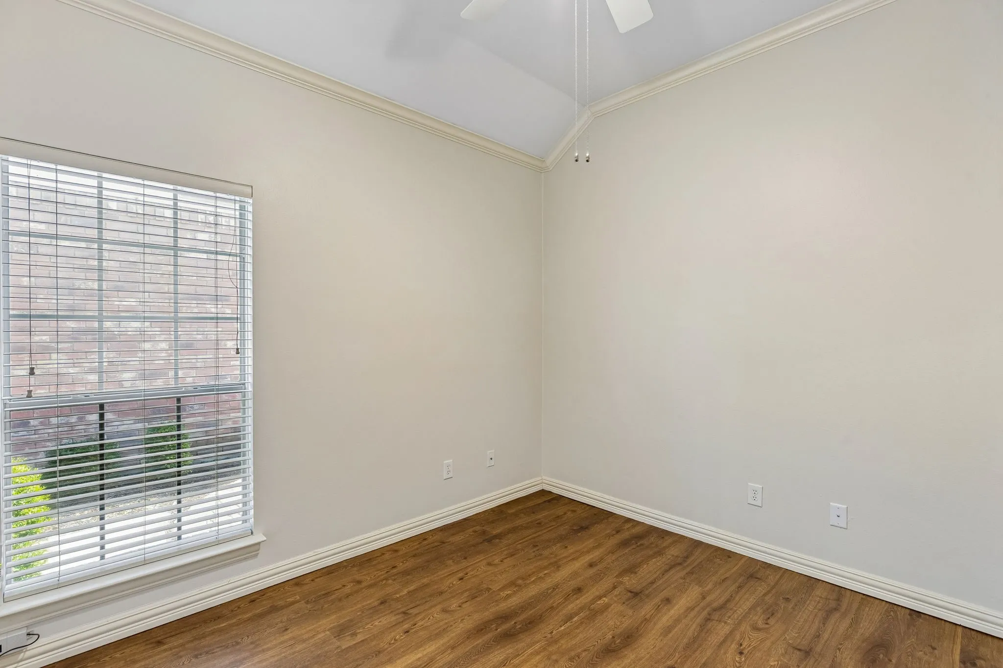 Room featuring wood-finish flooring, a vaulted ceiling, and crown molding