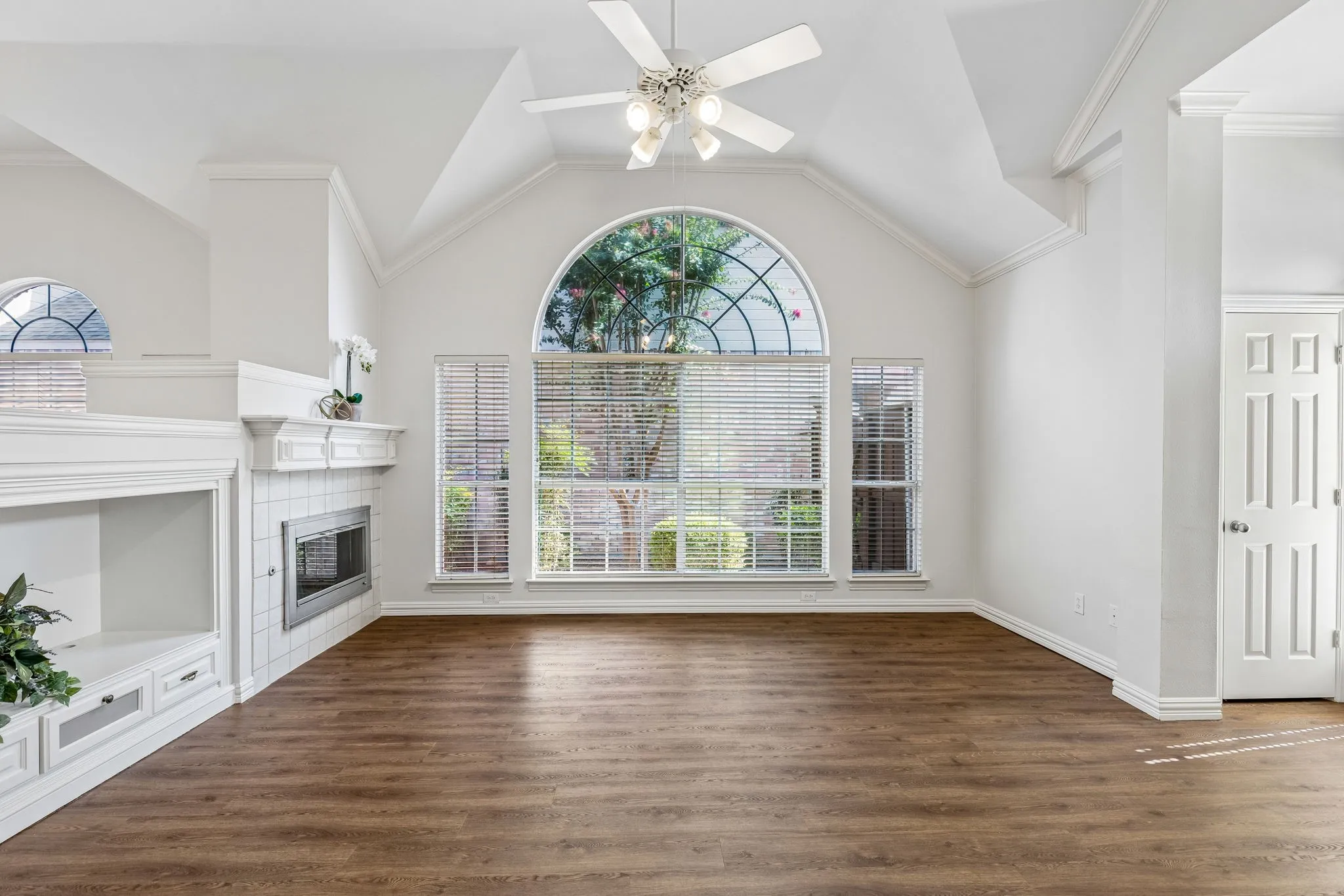 Living space featuring wood-finish flooring, vaulted ceilings, and a large arched window with transom detailing