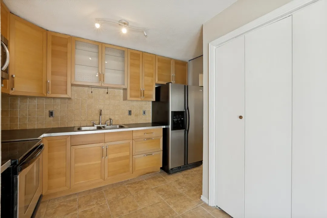 Kitchen featuring wood-finish cabinetry, stainless steel sink, tiled backsplash, track lighting, and stainless steel appliances