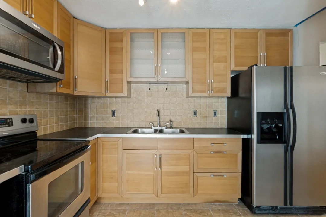 Kitchen featuring light wood cabinetry, dark countertops, and a tiled backsplash