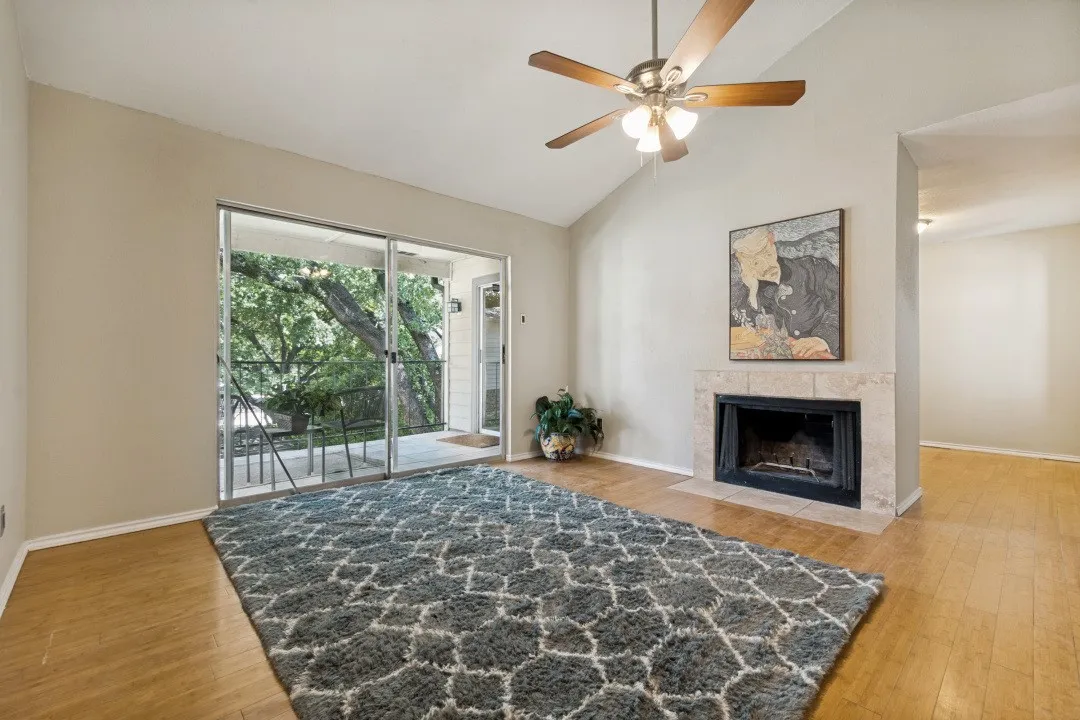 Living area featuring vaulted ceilings, wood-finish flooring, a tile-surround fireplace, and sliding glass doors opening to an outdoor patio with a dark metal railing