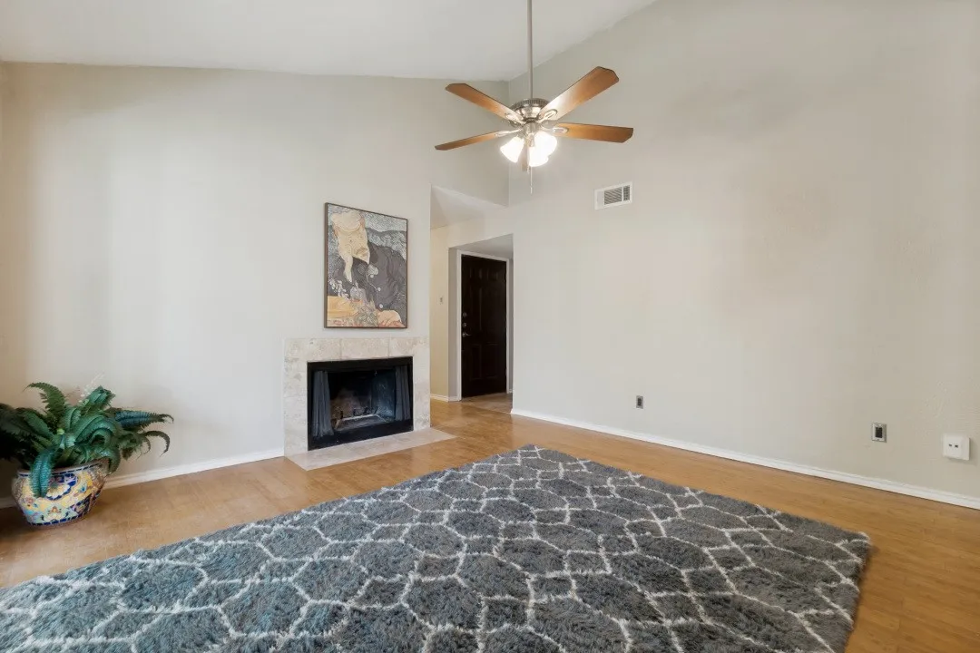 Vaulted ceiling living space featuring wood-finish flooring, a tile-surround fireplace, and a ceiling fan with integrated lighting