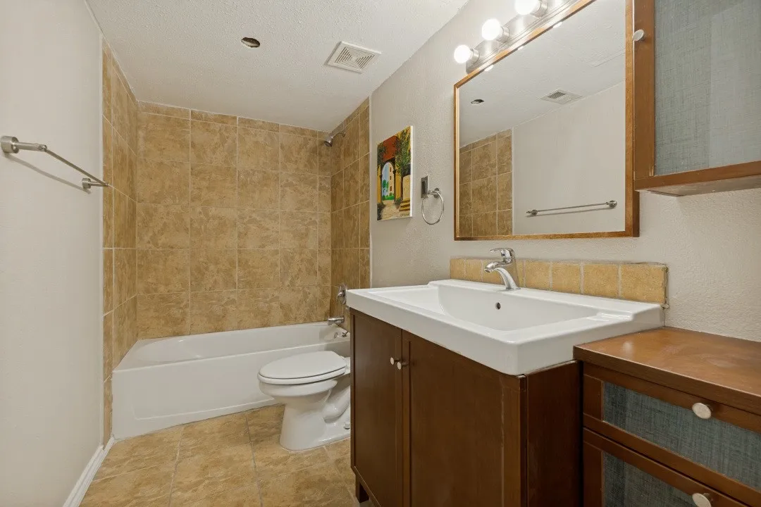 Bathroom featuring a full vanity with an integrated sink, framed mirror, and warm-toned tile flooring