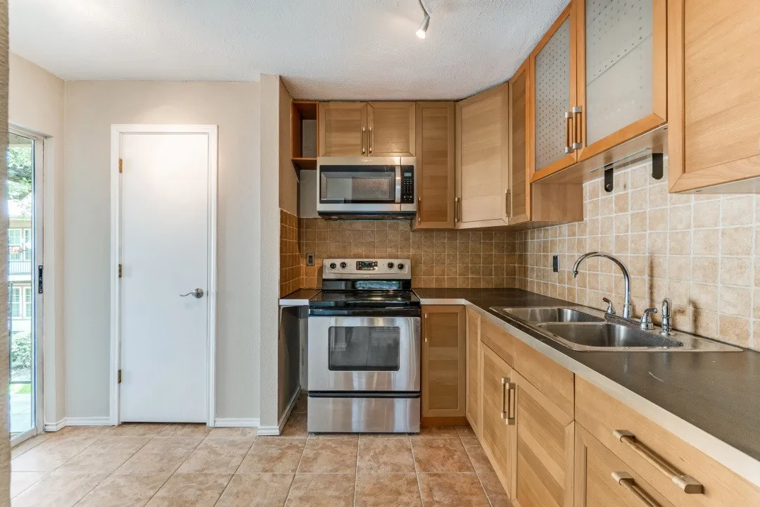 Kitchen featuring light wood cabinetry, stainless steel appliances, a tile backsplash, and tile flooring