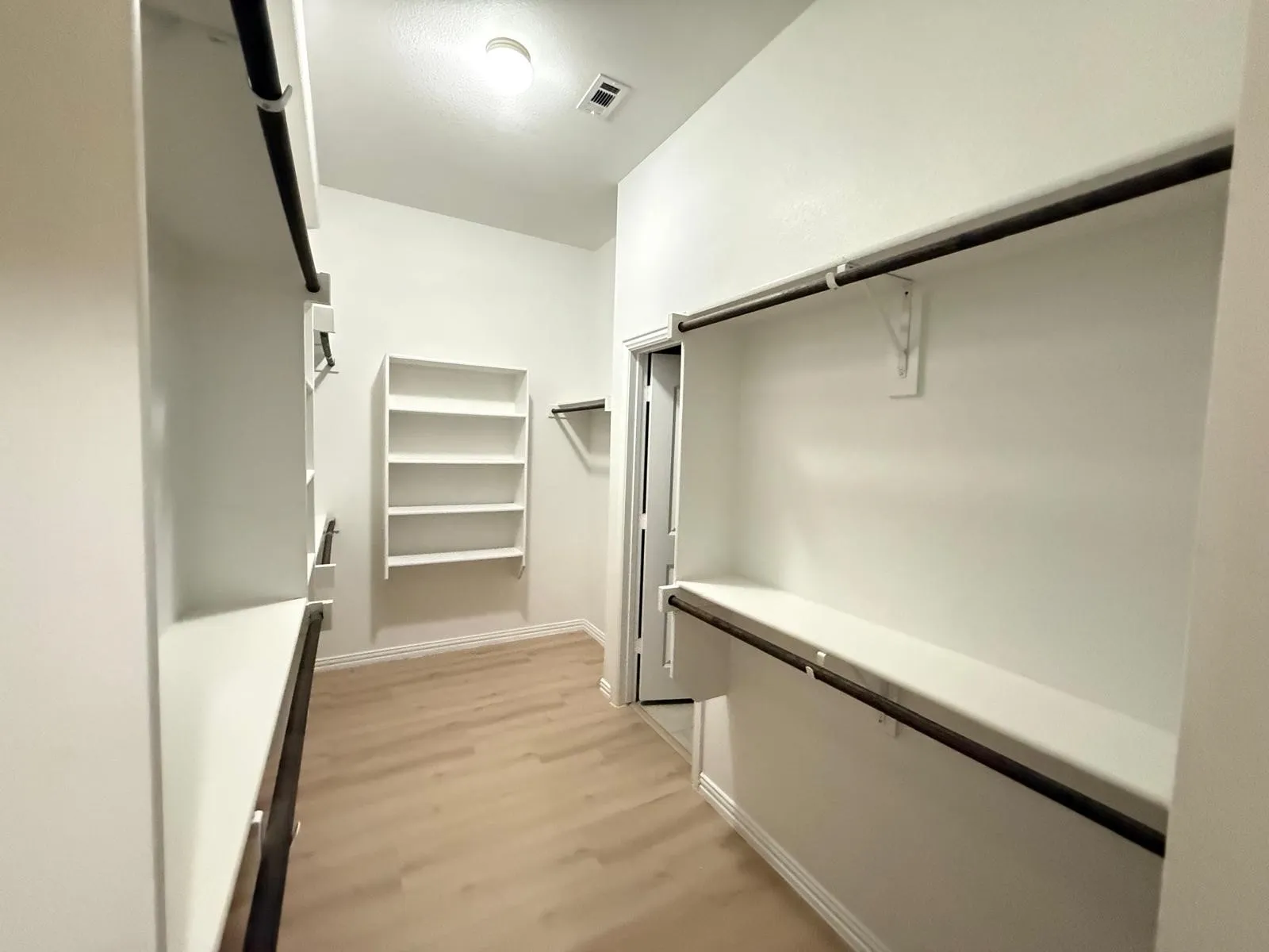 Expansive closet featuring wood-finish flooring, white built-in shelving, and multiple hanging rods