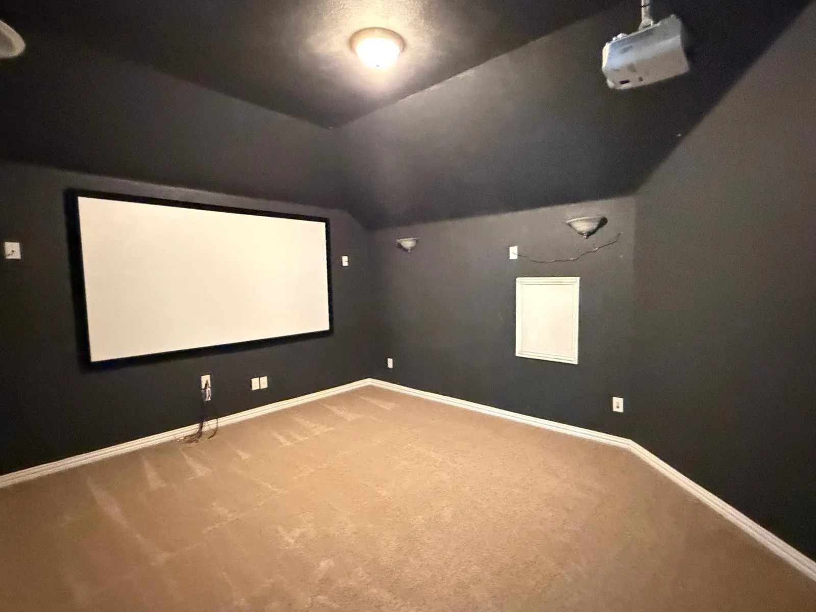 Dedicated media room featuring an expansive projection screen, wall-mounted projector, and dark painted walls