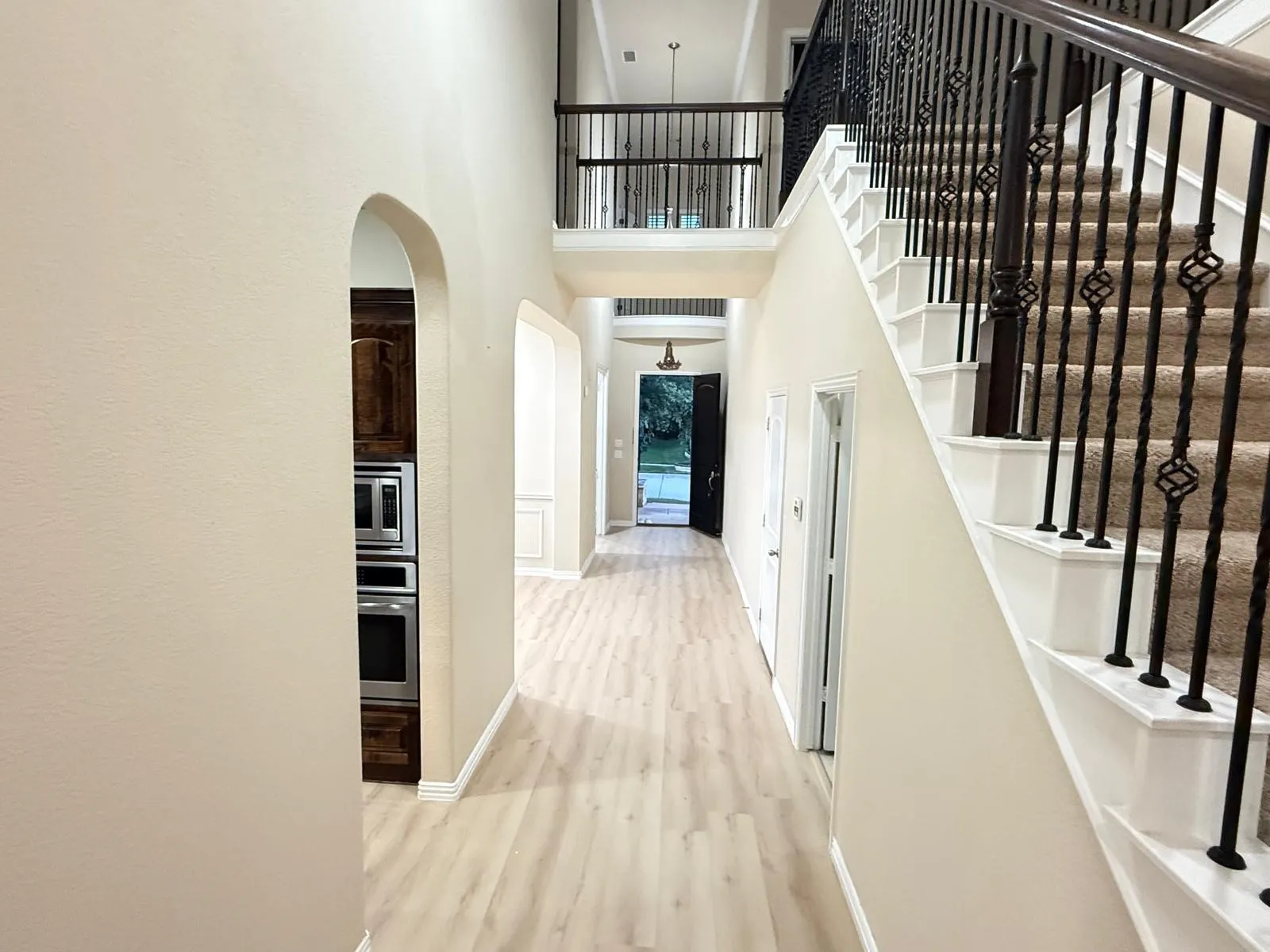 Grand foyer featuring a carpeted staircase with ornate wrought iron balusters and wood handrails, flanked by light wood-finish flooring