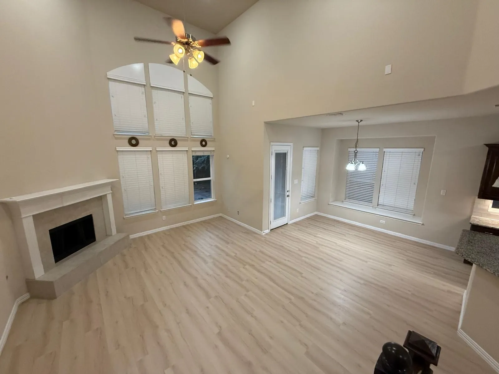 Spacious living area featuring high vaulted ceilings, light wood-finish flooring, and a fireplace with a stone mantel