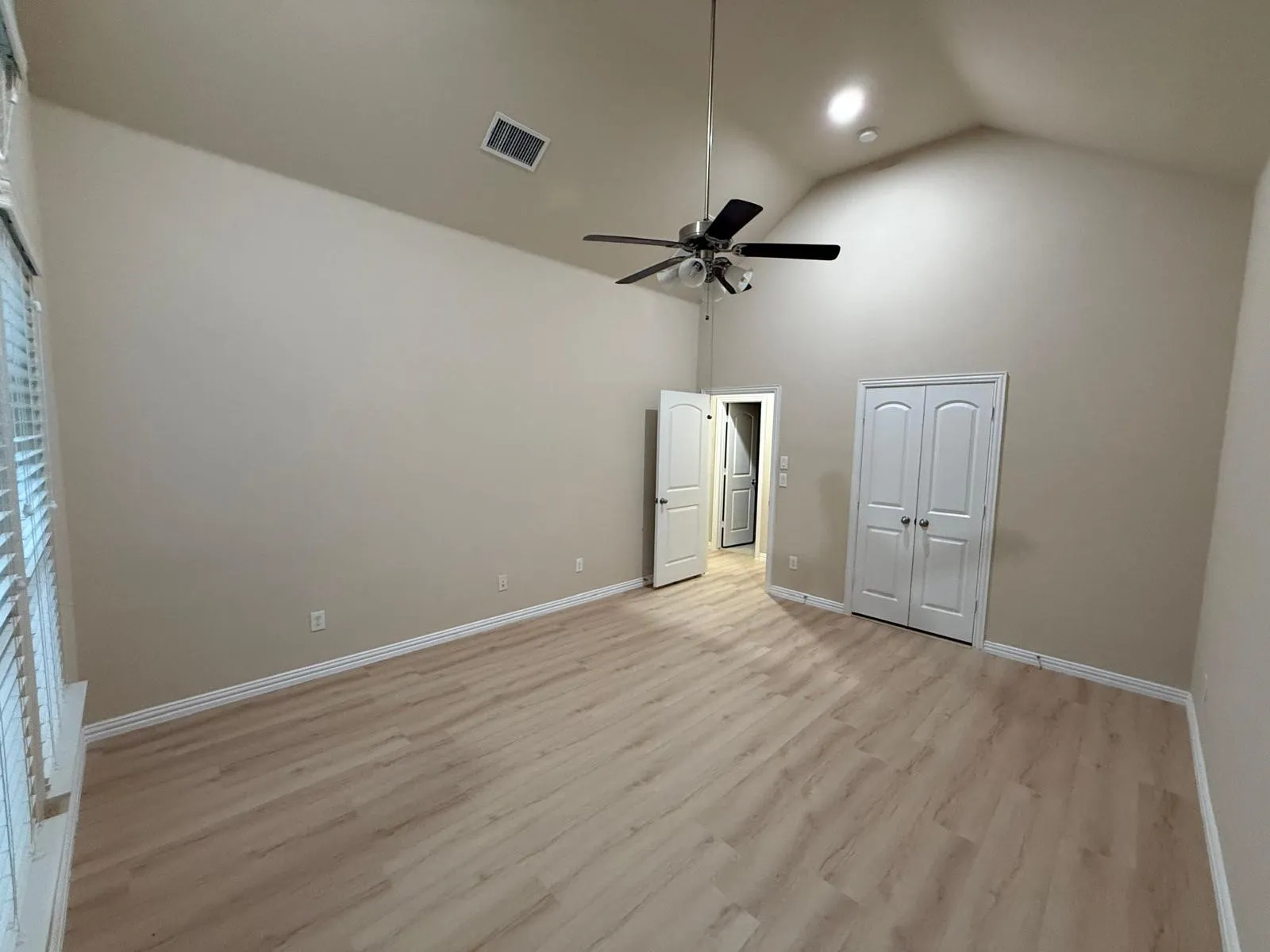 Spacious room featuring vaulted ceilings, light wood-finish flooring, a ceiling fan with integrated lighting, and multiple white paneled doors