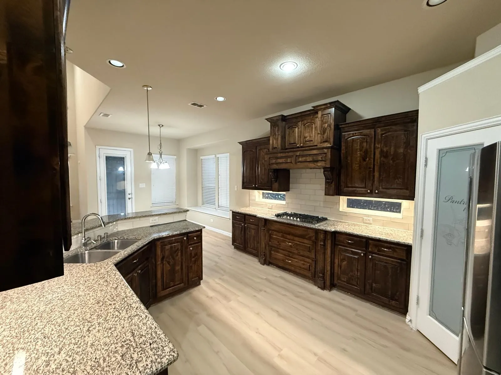 Spacious kitchen featuring dark wood cabinetry, granite countertops, subway tile backsplash, and light wood-finish flooring