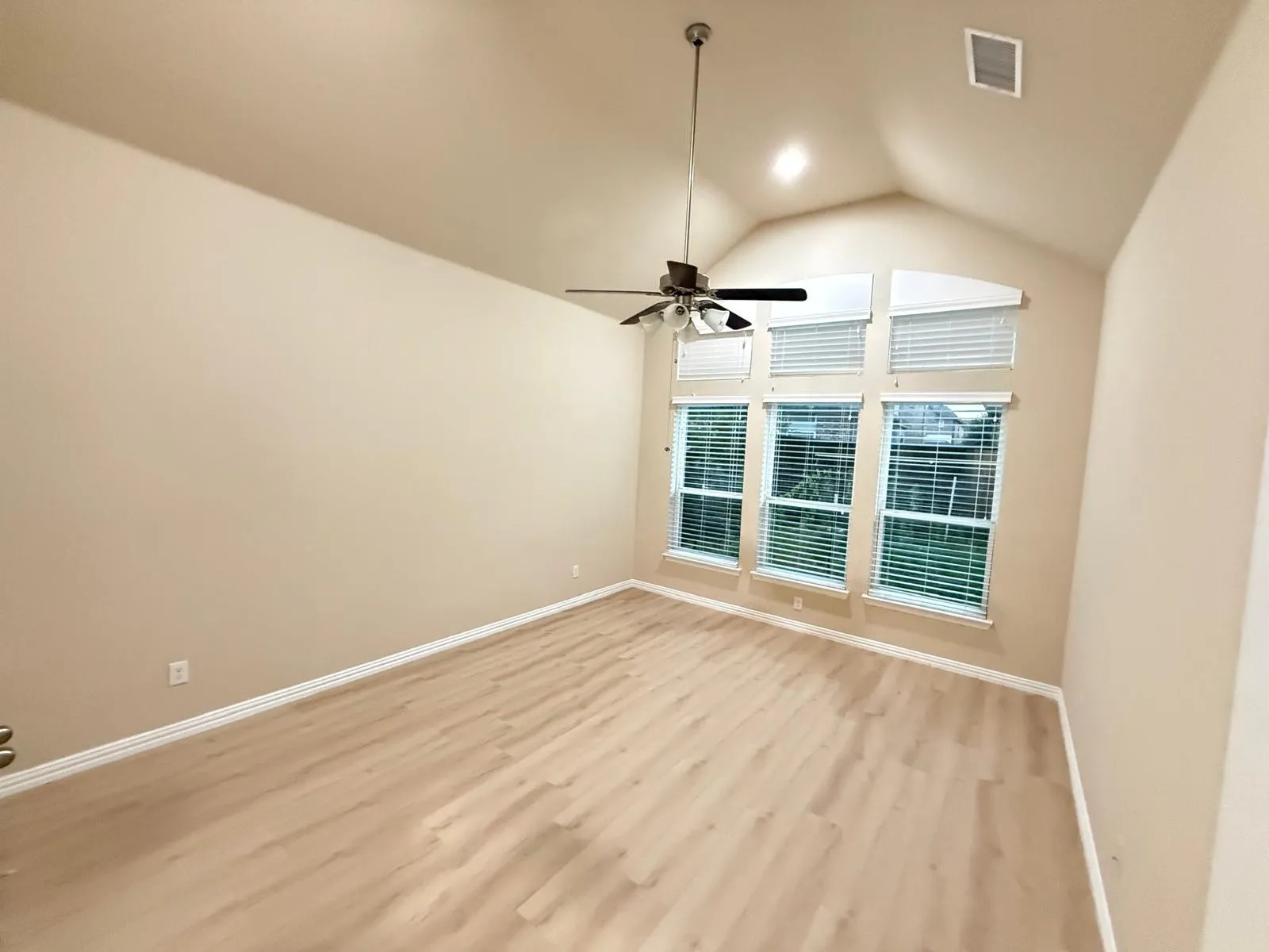 Spacious room featuring vaulted ceilings, an abundance of natural light from multiple windows, light wood-finish flooring, and a ceiling fan with integrated lighting