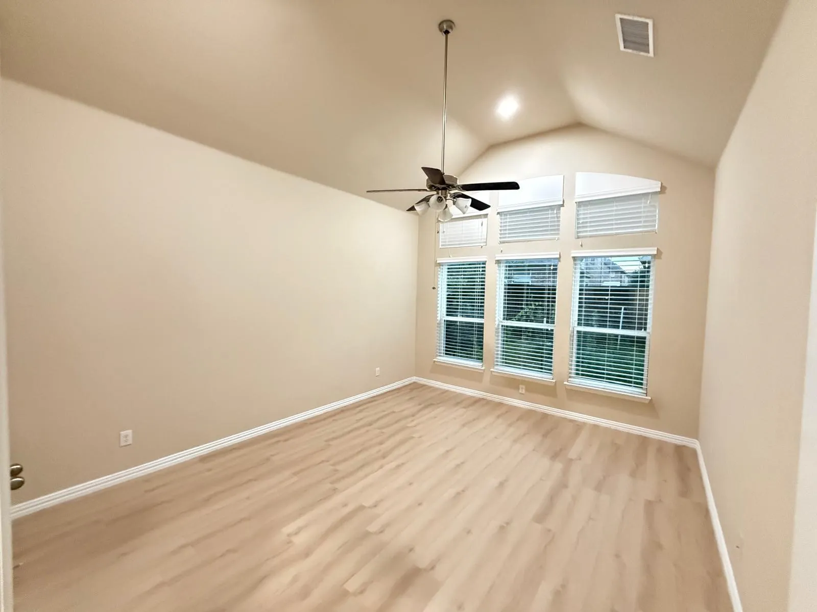 Vaulted ceiling room featuring light wood-finish flooring, a ceiling fan with light fixture, and a wall of three large windows