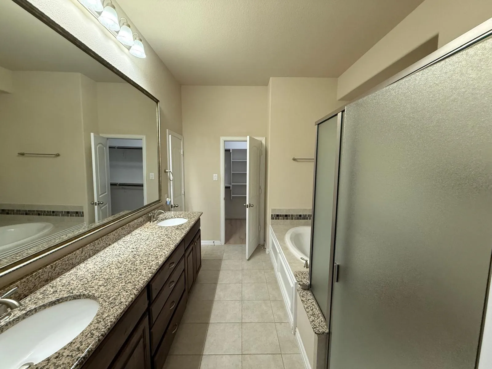 Bathroom featuring a long dual vanity with stone countertops, a full-width mirror, and an adjacent soaking tub with tile surround