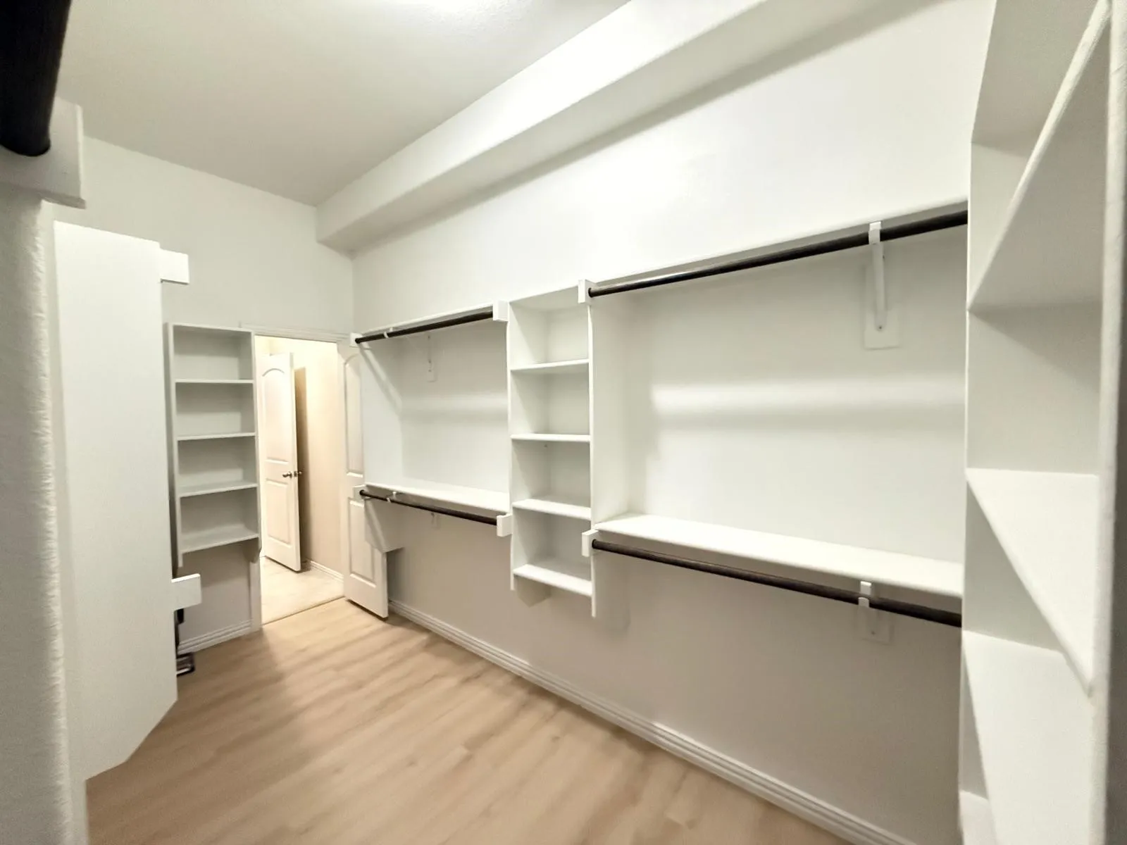 Spacious walk-in closet featuring light wood-finish flooring, white built-in shelving, and multiple hanging rods