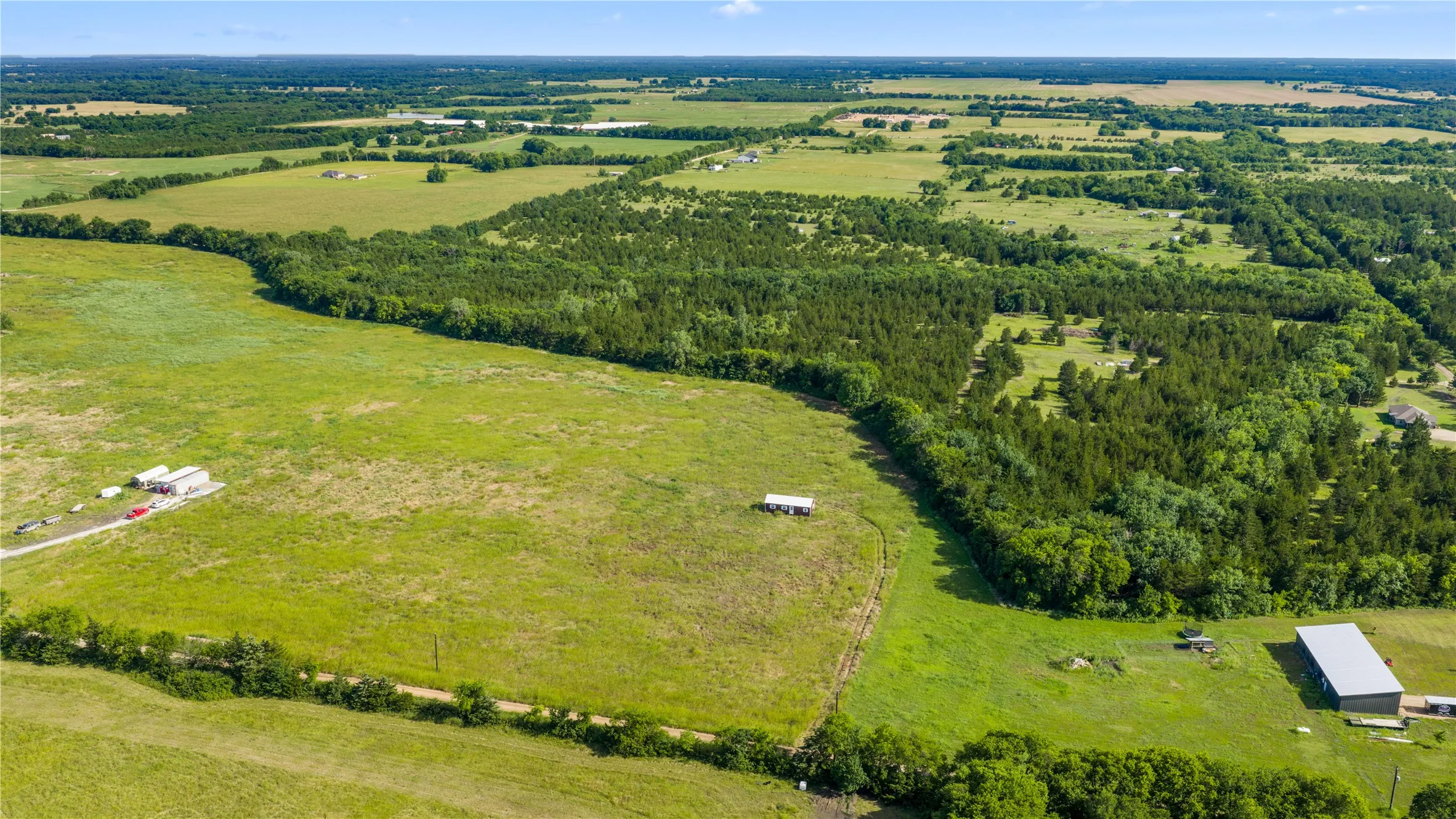 Expansive rural acreage featuring open fields, wooded sections, and a large metal outbuilding